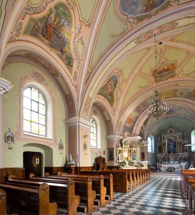 Zdjęcie nr 13: Kościół murowany, jednonawowy, na rzucie prostokąta, z późniejszymi dobudówkami. Prezbiterium usytuowane od północy, jednoprzęsłowe, węższe od korpusu, zamknięte półkolistą absydą. Do prezbiterium dobudowana zakrystia od wschodu oraz kaplica od zachodu poprzedzona niewielką kruchtą. Nawa główna trójprzęsłowa z partią wieżową niewyróżniającą się w bryle. Po bokach przęsła środkowego dostawione dwie kaplice na rzucie kwadratu: od wschodu Matki Boskiej Częstochowskiej, od zachodu św. Maksymiliana Marii Kolbego. Chór muzyczny wsparty na trzech arkadach. W prezbiterium sklepienie żaglaste, a w nawie krzyżowe, pozorne, oddzielone gurtami wychodzącymi z potężnych filarów przyściennych. Okna prostokątne, zamknięte półkoliście znajdują się w nawie, kaplicy przy prezbiterium, w wieży i w ścianach bocznych absydy. Natomiast w ścianach bocznych prezbiterium, na osi absydy i w kaplicach przy nawie okna koliste. Okna w większości wypełnione witrażami ze scenami figuralnymi, w innych ozdobne przeszklenia geometryczne. Fasada trójosiowa, na osi środkowej usytuowana wieża, delikatnie wystająca przed lico fasady, o podziałach ramowych, nakryta baniastym hełmem z dwukondygnacyjną latarnią. Osie boczne zwieńczone spływami wolutowymi. Dachy gontowe.

