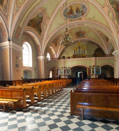 Zdjęcie nr 17: Kościół murowany, jednonawowy, na rzucie prostokąta, z późniejszymi dobudówkami. Prezbiterium usytuowane od północy, jednoprzęsłowe, węższe od korpusu, zamknięte półkolistą absydą. Do prezbiterium dobudowana zakrystia od wschodu oraz kaplica od zachodu poprzedzona niewielką kruchtą. Nawa główna trójprzęsłowa z partią wieżową niewyróżniającą się w bryle. Po bokach przęsła środkowego dostawione dwie kaplice na rzucie kwadratu: od wschodu Matki Boskiej Częstochowskiej, od zachodu św. Maksymiliana Marii Kolbego. Chór muzyczny wsparty na trzech arkadach. W prezbiterium sklepienie żaglaste, a w nawie krzyżowe, pozorne, oddzielone gurtami wychodzącymi z potężnych filarów przyściennych. Okna prostokątne, zamknięte półkoliście znajdują się w nawie, kaplicy przy prezbiterium, w wieży i w ścianach bocznych absydy. Natomiast w ścianach bocznych prezbiterium, na osi absydy i w kaplicach przy nawie okna koliste. Okna w większości wypełnione witrażami ze scenami figuralnymi, w innych ozdobne przeszklenia geometryczne. Fasada trójosiowa, na osi środkowej usytuowana wieża, delikatnie wystająca przed lico fasady, o podziałach ramowych, nakryta baniastym hełmem z dwukondygnacyjną latarnią. Osie boczne zwieńczone spływami wolutowymi. Dachy gontowe.

