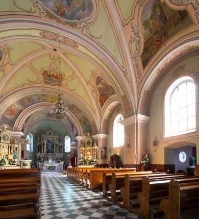 Zdjęcie nr 14: Kościół murowany, jednonawowy, na rzucie prostokąta, z późniejszymi dobudówkami. Prezbiterium usytuowane od północy, jednoprzęsłowe, węższe od korpusu, zamknięte półkolistą absydą. Do prezbiterium dobudowana zakrystia od wschodu oraz kaplica od zachodu poprzedzona niewielką kruchtą. Nawa główna trójprzęsłowa z partią wieżową niewyróżniającą się w bryle. Po bokach przęsła środkowego dostawione dwie kaplice na rzucie kwadratu: od wschodu Matki Boskiej Częstochowskiej, od zachodu św. Maksymiliana Marii Kolbego. Chór muzyczny wsparty na trzech arkadach. W prezbiterium sklepienie żaglaste, a w nawie krzyżowe, pozorne, oddzielone gurtami wychodzącymi z potężnych filarów przyściennych. Okna prostokątne, zamknięte półkoliście znajdują się w nawie, kaplicy przy prezbiterium, w wieży i w ścianach bocznych absydy. Natomiast w ścianach bocznych prezbiterium, na osi absydy i w kaplicach przy nawie okna koliste. Okna w większości wypełnione witrażami ze scenami figuralnymi, w innych ozdobne przeszklenia geometryczne. Fasada trójosiowa, na osi środkowej usytuowana wieża, delikatnie wystająca przed lico fasady, o podziałach ramowych, nakryta baniastym hełmem z dwukondygnacyjną latarnią. Osie boczne zwieńczone spływami wolutowymi. Dachy gontowe.

