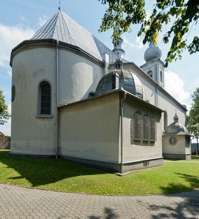 Zdjęcie nr 5: Kościół murowany, jednonawowy, na rzucie prostokąta, z późniejszymi dobudówkami. Prezbiterium usytuowane od północy, jednoprzęsłowe, węższe od korpusu, zamknięte półkolistą absydą. Do prezbiterium dobudowana zakrystia od wschodu oraz kaplica od zachodu poprzedzona niewielką kruchtą. Nawa główna trójprzęsłowa z partią wieżową niewyróżniającą się w bryle. Po bokach przęsła środkowego dostawione dwie kaplice na rzucie kwadratu: od wschodu Matki Boskiej Częstochowskiej, od zachodu św. Maksymiliana Marii Kolbego. Chór muzyczny wsparty na trzech arkadach. W prezbiterium sklepienie żaglaste, a w nawie krzyżowe, pozorne, oddzielone gurtami wychodzącymi z potężnych filarów przyściennych. Okna prostokątne, zamknięte półkoliście znajdują się w nawie, kaplicy przy prezbiterium, w wieży i w ścianach bocznych absydy. Natomiast w ścianach bocznych prezbiterium, na osi absydy i w kaplicach przy nawie okna koliste. Okna w większości wypełnione witrażami ze scenami figuralnymi, w innych ozdobne przeszklenia geometryczne. Fasada trójosiowa, na osi środkowej usytuowana wieża, delikatnie wystająca przed lico fasady, o podziałach ramowych, nakryta baniastym hełmem z dwukondygnacyjną latarnią. Osie boczne zwieńczone spływami wolutowymi. Dachy gontowe.

