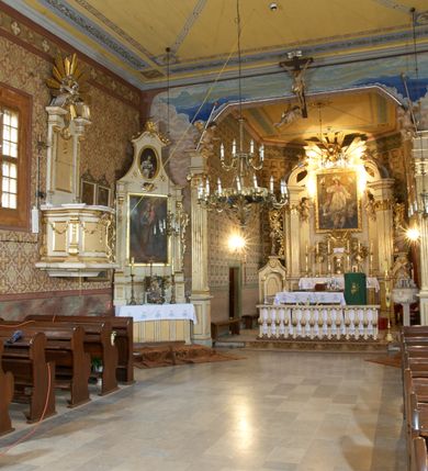 Zdjęcie nr 4: Kościół zlokalizowany na zachodnim krańcu wsi. Plac kościelny otoczony drewnianym płotem. W północno-wschodnim narożu drewniana dzwonnica.  
Kościół orientowany, drewniany, konstrukcji zrębowej, z wieżą na słup od zachodu, wejście główne od zachodu; wejścia boczne od południa przez kruchtę i od północy przez zakrystię. Prezbiterium zamknięte wielobocznie, nawa na rzucie prostokąta. Przy prezbiterium i nawie od północy zakrystia z przedsionkiem, przy nawie od południa kruchta. Wewnątrz stropy, podkreślone profilowanym gzymsem. Łuk tęczowy o wykroju prostokątnym ze ściętymi narożami, flankowany filarkami z belkowaniem; na nim późnobarokowy krucyfiks podtrzymywany przez aniołka, ponad belkowaniem aniołki dzierżące narzędzia Męki Pańskiej. Drugi łuk tęczowy usytuowany na granicy przedłużenia naw o podobnym wykroju. Chór muzyczny wsparty na dwóch żłobkowanych słupach o falistym przebiegu. Ściany nawy przeprute: od północy oknem o kształcie prostokąta, od południa trzema analogicznymi oknami i zwieńczone profilowanym gzymsem. Obramienia okienne fazowane, z nadokiennikami o wykroju w ośli grzbiet. Drzwi prowadzące do kruchty w kształcie prostokąta. Prezbiterium wzniesione o jeden stopień powyżej poziomu nawy, od południa przeprute dwoma prostokątnymi oknami. Od północy drzwi do zakrystii o kształcie stojącego prostokąta, od strony zakrystii profilowane. Zakrystia na planie prostokąta, przylegająca od północy do prezbiterium kościoła. Nawa i kruchta kryte dachem dwuspadowym, prezbiterium trójpołaciowym, opadającym ku wschodowi, zakrystia dachem pulpitowym. Przy wschodnim krańcu dachu nawy znajduje się wieżyczka na sygnaturkę. Dzwonnica drewniana, dwukondygnacyjna na planie zbliżonym do kwadratu. Nad pierwszą kondygnacją dach okapowy, a nad drugą czterospadowy, zwieńczony kulą z krzyżem. Na fasadzie kruchty wnęka z rzeźbą Matki Boskiej z Dzieciątkiem. 



