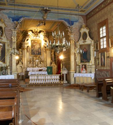 Zdjęcie nr 5: Kościół zlokalizowany na zachodnim krańcu wsi. Plac kościelny otoczony drewnianym płotem. W północno-wschodnim narożu drewniana dzwonnica.  
Kościół orientowany, drewniany, konstrukcji zrębowej, z wieżą na słup od zachodu, wejście główne od zachodu; wejścia boczne od południa przez kruchtę i od północy przez zakrystię. Prezbiterium zamknięte wielobocznie, nawa na rzucie prostokąta. Przy prezbiterium i nawie od północy zakrystia z przedsionkiem, przy nawie od południa kruchta. Wewnątrz stropy, podkreślone profilowanym gzymsem. Łuk tęczowy o wykroju prostokątnym ze ściętymi narożami, flankowany filarkami z belkowaniem; na nim późnobarokowy krucyfiks podtrzymywany przez aniołka, ponad belkowaniem aniołki dzierżące narzędzia Męki Pańskiej. Drugi łuk tęczowy usytuowany na granicy przedłużenia naw o podobnym wykroju. Chór muzyczny wsparty na dwóch żłobkowanych słupach o falistym przebiegu. Ściany nawy przeprute: od północy oknem o kształcie prostokąta, od południa trzema analogicznymi oknami i zwieńczone profilowanym gzymsem. Obramienia okienne fazowane, z nadokiennikami o wykroju w ośli grzbiet. Drzwi prowadzące do kruchty w kształcie prostokąta. Prezbiterium wzniesione o jeden stopień powyżej poziomu nawy, od południa przeprute dwoma prostokątnymi oknami. Od północy drzwi do zakrystii o kształcie stojącego prostokąta, od strony zakrystii profilowane. Zakrystia na planie prostokąta, przylegająca od północy do prezbiterium kościoła. Nawa i kruchta kryte dachem dwuspadowym, prezbiterium trójpołaciowym, opadającym ku wschodowi, zakrystia dachem pulpitowym. Przy wschodnim krańcu dachu nawy znajduje się wieżyczka na sygnaturkę. Dzwonnica drewniana, dwukondygnacyjna na planie zbliżonym do kwadratu. Nad pierwszą kondygnacją dach okapowy, a nad drugą czterospadowy, zwieńczony kulą z krzyżem. Na fasadzie kruchty wnęka z rzeźbą Matki Boskiej z Dzieciątkiem. 


