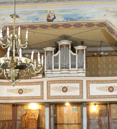 Zdjęcie nr 7: Kościół zlokalizowany na zachodnim krańcu wsi. Plac kościelny otoczony drewnianym płotem. W północno-wschodnim narożu drewniana dzwonnica.  
Kościół orientowany, drewniany, konstrukcji zrębowej, z wieżą na słup od zachodu, wejście główne od zachodu; wejścia boczne od południa przez kruchtę i od północy przez zakrystię. Prezbiterium zamknięte wielobocznie, nawa na rzucie prostokąta. Przy prezbiterium i nawie od północy zakrystia z przedsionkiem, przy nawie od południa kruchta. Wewnątrz stropy, podkreślone profilowanym gzymsem. Łuk tęczowy o wykroju prostokątnym ze ściętymi narożami, flankowany filarkami z belkowaniem; na nim późnobarokowy krucyfiks podtrzymywany przez aniołka, ponad belkowaniem aniołki dzierżące narzędzia Męki Pańskiej. Drugi łuk tęczowy usytuowany na granicy przedłużenia naw o podobnym wykroju. Chór muzyczny wsparty na dwóch żłobkowanych słupach o falistym przebiegu. Ściany nawy przeprute: od północy oknem o kształcie prostokąta, od południa trzema analogicznymi oknami i zwieńczone profilowanym gzymsem. Obramienia okienne fazowane, z nadokiennikami o wykroju w ośli grzbiet. Drzwi prowadzące do kruchty w kształcie prostokąta. Prezbiterium wzniesione o jeden stopień powyżej poziomu nawy, od południa przeprute dwoma prostokątnymi oknami. Od północy drzwi do zakrystii o kształcie stojącego prostokąta, od strony zakrystii profilowane. Zakrystia na planie prostokąta, przylegająca od północy do prezbiterium kościoła. Nawa i kruchta kryte dachem dwuspadowym, prezbiterium trójpołaciowym, opadającym ku wschodowi, zakrystia dachem pulpitowym. Przy wschodnim krańcu dachu nawy znajduje się wieżyczka na sygnaturkę. Dzwonnica drewniana, dwukondygnacyjna na planie zbliżonym do kwadratu. Nad pierwszą kondygnacją dach okapowy, a nad drugą czterospadowy, zwieńczony kulą z krzyżem. Na fasadzie kruchty wnęka z rzeźbą Matki Boskiej z Dzieciątkiem. 


