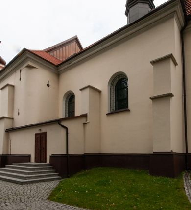 Zdjęcie nr 32: Kościół orientowany, murowany, jednonawowy z prezbiterium zakończonym wielobocznie. Wschodnia część węższa, prostokątna, zachodnia szersza, trójnawowa, halowa. Do prezbiterium od północy przylega zakrystia, do wschodniej części korpusu przybudówka, od zachodu kruchta. Ściany nawy dzielą pilastry. Prezbiterium sklepione krzyżowo, absyda konchowo z lunetami, nawy kolebkowo z lunetami. Od zachodu chór wsparty na dwóch czworobocznych słupach. Jego parapet jest wybrzuszony w części środkowej, ażurowy, zakończony u dołu listwą wycinaną w formie stylizowanych listków. W prezbiterium jedno okno w kształcie stojącego prostokąta zamknięte łukiem pełnym i jedno ślepe, zamknięte łukiem ostrym. Od strony  północnej do zakrystii dwa okna zamknięte łukiem odcinkowym i cztery prostokątne, dwa okna zamknięte łukiem pełnym do zachodniej części nawy; od strony południowej pięć okien zamkniętych łukiem pełnym. Główne wejście od zachodu, drugie od południa, kolejne do  zakrystii, portal z prezbiterium do zakrystii, z czarnego marmuru. Fasada dwuwieżowa, z kruchtą, do której prowadzi ciąg schodów. Kruchta prostopadłościenna, z dachem dwuspadowym, z portalem w kształcie prostokąta zamkniętego łukiem pełnym na osi między oknami powtarzającymi ten kształt. Nad kondygnacją trójkątny przyczółek z krzyżem łacińskim. Fasada dwukondygnacyjna, z wieżami wtopionymi w lico. Pierwsza kondygnacja gładka, flankowana szkarpami, zamknięta gzymsem, druga również niemal gładka, z zegarem na środku i małymi oknami w partii wież. Na osi trójkątny przyczółek. Elewacje obiega cokół, wspierają szkarpy – najgęściej ustawione wokół prezbiterium. Dachy naw dwuspadowe, nad prezbiterium dach zakończony wielobocznie, nad zakrystią pulpitowy; na kalenicy wieżyczka na sygnaturkę, wieże zakończone rozbudowanymi hełmami. 
We wnętrzu na uwagę zasługują chrzcielnica z czarnego marmuru z XVII wieku, obraz św. Izydora w prawym, bocznym ołtarzu według tradycji pędzla Michała Stachowicza i późnobarokowe ołtarze. Prowadzący do zakrystii portal z czarnego marmuru i ołtarz boczny lewy Ukrzyżowania pochodzą, według niektórych przekazów, z krakowskiego kościoła Wszystkich Świętych. 
