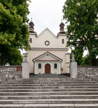 Zdjęcie nr 2: Kościół orientowany, murowany, jednonawowy z prezbiterium zakończonym wielobocznie. Wschodnia część węższa, prostokątna, zachodnia szersza, trójnawowa, halowa. Do prezbiterium od północy przylega zakrystia, do wschodniej części korpusu przybudówka, od zachodu kruchta. Ściany nawy dzielą pilastry. Prezbiterium sklepione krzyżowo, absyda konchowo z lunetami, nawy kolebkowo z lunetami. Od zachodu chór wsparty na dwóch czworobocznych słupach. Jego parapet jest wybrzuszony w części środkowej, ażurowy, zakończony u dołu listwą wycinaną w formie stylizowanych listków. W prezbiterium jedno okno w kształcie stojącego prostokąta zamknięte łukiem pełnym i jedno ślepe, zamknięte łukiem ostrym. Od strony  północnej do zakrystii dwa okna zamknięte łukiem odcinkowym i cztery prostokątne, dwa okna zamknięte łukiem pełnym do zachodniej części nawy; od strony południowej pięć okien zamkniętych łukiem pełnym. Główne wejście od zachodu, drugie od południa, kolejne do  zakrystii, portal z prezbiterium do zakrystii, z czarnego marmuru. Fasada dwuwieżowa, z kruchtą, do której prowadzi ciąg schodów. Kruchta prostopadłościenna, z dachem dwuspadowym, z portalem w kształcie prostokąta zamkniętego łukiem pełnym na osi między oknami powtarzającymi ten kształt. Nad kondygnacją trójkątny przyczółek z krzyżem łacińskim. Fasada dwukondygnacyjna, z wieżami wtopionymi w lico. Pierwsza kondygnacja gładka, flankowana szkarpami, zamknięta gzymsem, druga również niemal gładka, z zegarem na środku i małymi oknami w partii wież. Na osi trójkątny przyczółek. Elewacje obiega cokół, wspierają szkarpy – najgęściej ustawione wokół prezbiterium. Dachy naw dwuspadowe, nad prezbiterium dach zakończony wielobocznie, nad zakrystią pulpitowy; na kalenicy wieżyczka na sygnaturkę, wieże zakończone rozbudowanymi hełmami. 
We wnętrzu na uwagę zasługują chrzcielnica z czarnego marmuru z XVII wieku, obraz św. Izydora w prawym, bocznym ołtarzu według tradycji pędzla Michała Stachowicza i późnobarokowe ołtarze. Prowadzący do zakrystii portal z czarnego marmuru i ołtarz boczny lewy Ukrzyżowania pochodzą, według niektórych przekazów, z krakowskiego kościoła Wszystkich Świętych. 
