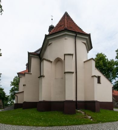Zdjęcie nr 3: Kościół orientowany, murowany, jednonawowy z prezbiterium zakończonym wielobocznie. Wschodnia część węższa, prostokątna, zachodnia szersza, trójnawowa, halowa. Do prezbiterium od północy przylega zakrystia, do wschodniej części korpusu przybudówka, od zachodu kruchta. Ściany nawy dzielą pilastry. Prezbiterium sklepione krzyżowo, absyda konchowo z lunetami, nawy kolebkowo z lunetami. Od zachodu chór wsparty na dwóch czworobocznych słupach. Jego parapet jest wybrzuszony w części środkowej, ażurowy, zakończony u dołu listwą wycinaną w formie stylizowanych listków. W prezbiterium jedno okno w kształcie stojącego prostokąta zamknięte łukiem pełnym i jedno ślepe, zamknięte łukiem ostrym. Od strony  północnej do zakrystii dwa okna zamknięte łukiem odcinkowym i cztery prostokątne, dwa okna zamknięte łukiem pełnym do zachodniej części nawy; od strony południowej pięć okien zamkniętych łukiem pełnym. Główne wejście od zachodu, drugie od południa, kolejne do  zakrystii, portal z prezbiterium do zakrystii, z czarnego marmuru. Fasada dwuwieżowa, z kruchtą, do której prowadzi ciąg schodów. Kruchta prostopadłościenna, z dachem dwuspadowym, z portalem w kształcie prostokąta zamkniętego łukiem pełnym na osi między oknami powtarzającymi ten kształt. Nad kondygnacją trójkątny przyczółek z krzyżem łacińskim. Fasada dwukondygnacyjna, z wieżami wtopionymi w lico. Pierwsza kondygnacja gładka, flankowana szkarpami, zamknięta gzymsem, druga również niemal gładka, z zegarem na środku i małymi oknami w partii wież. Na osi trójkątny przyczółek. Elewacje obiega cokół, wspierają szkarpy – najgęściej ustawione wokół prezbiterium. Dachy naw dwuspadowe, nad prezbiterium dach zakończony wielobocznie, nad zakrystią pulpitowy; na kalenicy wieżyczka na sygnaturkę, wieże zakończone rozbudowanymi hełmami. 
We wnętrzu na uwagę zasługują chrzcielnica z czarnego marmuru z XVII wieku, obraz św. Izydora w prawym, bocznym ołtarzu według tradycji pędzla Michała Stachowicza i późnobarokowe ołtarze. Prowadzący do zakrystii portal z czarnego marmuru i ołtarz boczny lewy Ukrzyżowania pochodzą, według niektórych przekazów, z krakowskiego kościoła Wszystkich Świętych. 
