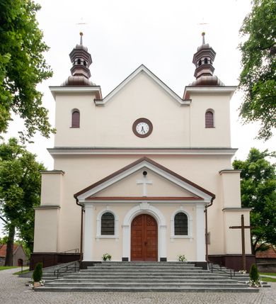 Zdjęcie nr 13: Kościół orientowany, murowany, jednonawowy z prezbiterium zakończonym wielobocznie. Wschodnia część węższa, prostokątna, zachodnia szersza, trójnawowa, halowa. Do prezbiterium od północy przylega zakrystia, do wschodniej części korpusu przybudówka, od zachodu kruchta. Ściany nawy dzielą pilastry. Prezbiterium sklepione krzyżowo, absyda konchowo z lunetami, nawy kolebkowo z lunetami. Od zachodu chór wsparty na dwóch czworobocznych słupach. Jego parapet jest wybrzuszony w części środkowej, ażurowy, zakończony u dołu listwą wycinaną w formie stylizowanych listków. W prezbiterium jedno okno w kształcie stojącego prostokąta zamknięte łukiem pełnym i jedno ślepe, zamknięte łukiem ostrym. Od strony  północnej do zakrystii dwa okna zamknięte łukiem odcinkowym i cztery prostokątne, dwa okna zamknięte łukiem pełnym do zachodniej części nawy; od strony południowej pięć okien zamkniętych łukiem pełnym. Główne wejście od zachodu, drugie od południa, kolejne do  zakrystii, portal z prezbiterium do zakrystii, z czarnego marmuru. Fasada dwuwieżowa, z kruchtą, do której prowadzi ciąg schodów. Kruchta prostopadłościenna, z dachem dwuspadowym, z portalem w kształcie prostokąta zamkniętego łukiem pełnym na osi między oknami powtarzającymi ten kształt. Nad kondygnacją trójkątny przyczółek z krzyżem łacińskim. Fasada dwukondygnacyjna, z wieżami wtopionymi w lico. Pierwsza kondygnacja gładka, flankowana szkarpami, zamknięta gzymsem, druga również niemal gładka, z zegarem na środku i małymi oknami w partii wież. Na osi trójkątny przyczółek. Elewacje obiega cokół, wspierają szkarpy – najgęściej ustawione wokół prezbiterium. Dachy naw dwuspadowe, nad prezbiterium dach zakończony wielobocznie, nad zakrystią pulpitowy; na kalenicy wieżyczka na sygnaturkę, wieże zakończone rozbudowanymi hełmami. 
We wnętrzu na uwagę zasługują chrzcielnica z czarnego marmuru z XVII wieku, obraz św. Izydora w prawym, bocznym ołtarzu według tradycji pędzla Michała Stachowicza i późnobarokowe ołtarze. Prowadzący do zakrystii portal z czarnego marmuru i ołtarz boczny lewy Ukrzyżowania pochodzą, według niektórych przekazów, z krakowskiego kościoła Wszystkich Świętych. 
