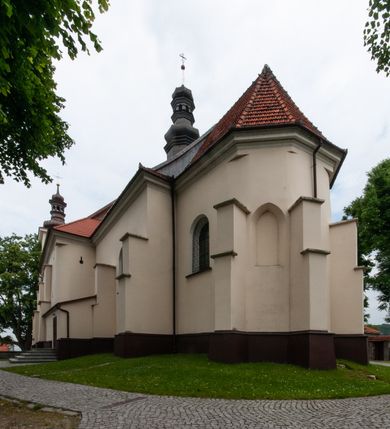 Zdjęcie nr 30: Kościół orientowany, murowany, jednonawowy z prezbiterium zakończonym wielobocznie. Wschodnia część węższa, prostokątna, zachodnia szersza, trójnawowa, halowa. Do prezbiterium od północy przylega zakrystia, do wschodniej części korpusu przybudówka, od zachodu kruchta. Ściany nawy dzielą pilastry. Prezbiterium sklepione krzyżowo, absyda konchowo z lunetami, nawy kolebkowo z lunetami. Od zachodu chór wsparty na dwóch czworobocznych słupach. Jego parapet jest wybrzuszony w części środkowej, ażurowy, zakończony u dołu listwą wycinaną w formie stylizowanych listków. W prezbiterium jedno okno w kształcie stojącego prostokąta zamknięte łukiem pełnym i jedno ślepe, zamknięte łukiem ostrym. Od strony  północnej do zakrystii dwa okna zamknięte łukiem odcinkowym i cztery prostokątne, dwa okna zamknięte łukiem pełnym do zachodniej części nawy; od strony południowej pięć okien zamkniętych łukiem pełnym. Główne wejście od zachodu, drugie od południa, kolejne do  zakrystii, portal z prezbiterium do zakrystii, z czarnego marmuru. Fasada dwuwieżowa, z kruchtą, do której prowadzi ciąg schodów. Kruchta prostopadłościenna, z dachem dwuspadowym, z portalem w kształcie prostokąta zamkniętego łukiem pełnym na osi między oknami powtarzającymi ten kształt. Nad kondygnacją trójkątny przyczółek z krzyżem łacińskim. Fasada dwukondygnacyjna, z wieżami wtopionymi w lico. Pierwsza kondygnacja gładka, flankowana szkarpami, zamknięta gzymsem, druga również niemal gładka, z zegarem na środku i małymi oknami w partii wież. Na osi trójkątny przyczółek. Elewacje obiega cokół, wspierają szkarpy – najgęściej ustawione wokół prezbiterium. Dachy naw dwuspadowe, nad prezbiterium dach zakończony wielobocznie, nad zakrystią pulpitowy; na kalenicy wieżyczka na sygnaturkę, wieże zakończone rozbudowanymi hełmami. 
We wnętrzu na uwagę zasługują chrzcielnica z czarnego marmuru z XVII wieku, obraz św. Izydora w prawym, bocznym ołtarzu według tradycji pędzla Michała Stachowicza i późnobarokowe ołtarze. Prowadzący do zakrystii portal z czarnego marmuru i ołtarz boczny lewy Ukrzyżowania pochodzą, według niektórych przekazów, z krakowskiego kościoła Wszystkich Świętych. 
