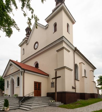 Zdjęcie nr 29: Kościół orientowany, murowany, jednonawowy z prezbiterium zakończonym wielobocznie. Wschodnia część węższa, prostokątna, zachodnia szersza, trójnawowa, halowa. Do prezbiterium od północy przylega zakrystia, do wschodniej części korpusu przybudówka, od zachodu kruchta. Ściany nawy dzielą pilastry. Prezbiterium sklepione krzyżowo, absyda konchowo z lunetami, nawy kolebkowo z lunetami. Od zachodu chór wsparty na dwóch czworobocznych słupach. Jego parapet jest wybrzuszony w części środkowej, ażurowy, zakończony u dołu listwą wycinaną w formie stylizowanych listków. W prezbiterium jedno okno w kształcie stojącego prostokąta zamknięte łukiem pełnym i jedno ślepe, zamknięte łukiem ostrym. Od strony  północnej do zakrystii dwa okna zamknięte łukiem odcinkowym i cztery prostokątne, dwa okna zamknięte łukiem pełnym do zachodniej części nawy; od strony południowej pięć okien zamkniętych łukiem pełnym. Główne wejście od zachodu, drugie od południa, kolejne do  zakrystii, portal z prezbiterium do zakrystii, z czarnego marmuru. Fasada dwuwieżowa, z kruchtą, do której prowadzi ciąg schodów. Kruchta prostopadłościenna, z dachem dwuspadowym, z portalem w kształcie prostokąta zamkniętego łukiem pełnym na osi między oknami powtarzającymi ten kształt. Nad kondygnacją trójkątny przyczółek z krzyżem łacińskim. Fasada dwukondygnacyjna, z wieżami wtopionymi w lico. Pierwsza kondygnacja gładka, flankowana szkarpami, zamknięta gzymsem, druga również niemal gładka, z zegarem na środku i małymi oknami w partii wież. Na osi trójkątny przyczółek. Elewacje obiega cokół, wspierają szkarpy – najgęściej ustawione wokół prezbiterium. Dachy naw dwuspadowe, nad prezbiterium dach zakończony wielobocznie, nad zakrystią pulpitowy; na kalenicy wieżyczka na sygnaturkę, wieże zakończone rozbudowanymi hełmami. 
We wnętrzu na uwagę zasługują chrzcielnica z czarnego marmuru z XVII wieku, obraz św. Izydora w prawym, bocznym ołtarzu według tradycji pędzla Michała Stachowicza i późnobarokowe ołtarze. Prowadzący do zakrystii portal z czarnego marmuru i ołtarz boczny lewy Ukrzyżowania pochodzą, według niektórych przekazów, z krakowskiego kościoła Wszystkich Świętych. 
