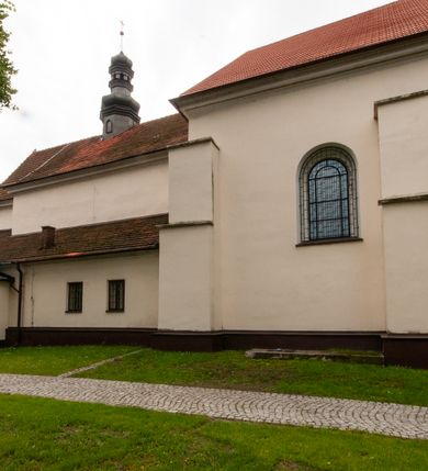 Zdjęcie nr 10: Kościół orientowany, murowany, jednonawowy z prezbiterium zakończonym wielobocznie. Wschodnia część węższa, prostokątna, zachodnia szersza, trójnawowa, halowa. Do prezbiterium od północy przylega zakrystia, do wschodniej części korpusu przybudówka, od zachodu kruchta. Ściany nawy dzielą pilastry. Prezbiterium sklepione krzyżowo, absyda konchowo z lunetami, nawy kolebkowo z lunetami. Od zachodu chór wsparty na dwóch czworobocznych słupach. Jego parapet jest wybrzuszony w części środkowej, ażurowy, zakończony u dołu listwą wycinaną w formie stylizowanych listków. W prezbiterium jedno okno w kształcie stojącego prostokąta zamknięte łukiem pełnym i jedno ślepe, zamknięte łukiem ostrym. Od strony  północnej do zakrystii dwa okna zamknięte łukiem odcinkowym i cztery prostokątne, dwa okna zamknięte łukiem pełnym do zachodniej części nawy; od strony południowej pięć okien zamkniętych łukiem pełnym. Główne wejście od zachodu, drugie od południa, kolejne do  zakrystii, portal z prezbiterium do zakrystii, z czarnego marmuru. Fasada dwuwieżowa, z kruchtą, do której prowadzi ciąg schodów. Kruchta prostopadłościenna, z dachem dwuspadowym, z portalem w kształcie prostokąta zamkniętego łukiem pełnym na osi między oknami powtarzającymi ten kształt. Nad kondygnacją trójkątny przyczółek z krzyżem łacińskim. Fasada dwukondygnacyjna, z wieżami wtopionymi w lico. Pierwsza kondygnacja gładka, flankowana szkarpami, zamknięta gzymsem, druga również niemal gładka, z zegarem na środku i małymi oknami w partii wież. Na osi trójkątny przyczółek. Elewacje obiega cokół, wspierają szkarpy – najgęściej ustawione wokół prezbiterium. Dachy naw dwuspadowe, nad prezbiterium dach zakończony wielobocznie, nad zakrystią pulpitowy; na kalenicy wieżyczka na sygnaturkę, wieże zakończone rozbudowanymi hełmami. 
We wnętrzu na uwagę zasługują chrzcielnica z czarnego marmuru z XVII wieku, obraz św. Izydora w prawym, bocznym ołtarzu według tradycji pędzla Michała Stachowicza i późnobarokowe ołtarze. Prowadzący do zakrystii portal z czarnego marmuru i ołtarz boczny lewy Ukrzyżowania pochodzą, według niektórych przekazów, z krakowskiego kościoła Wszystkich Świętych. 
