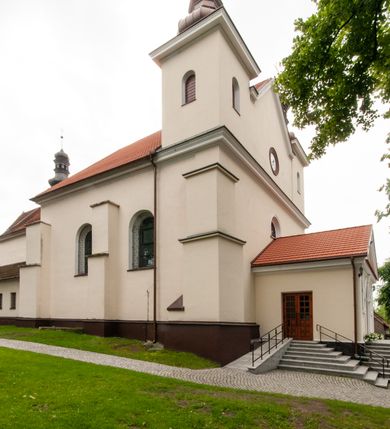 Zdjęcie nr 11: Kościół orientowany, murowany, jednonawowy z prezbiterium zakończonym wielobocznie. Wschodnia część węższa, prostokątna, zachodnia szersza, trójnawowa, halowa. Do prezbiterium od północy przylega zakrystia, do wschodniej części korpusu przybudówka, od zachodu kruchta. Ściany nawy dzielą pilastry. Prezbiterium sklepione krzyżowo, absyda konchowo z lunetami, nawy kolebkowo z lunetami. Od zachodu chór wsparty na dwóch czworobocznych słupach. Jego parapet jest wybrzuszony w części środkowej, ażurowy, zakończony u dołu listwą wycinaną w formie stylizowanych listków. W prezbiterium jedno okno w kształcie stojącego prostokąta zamknięte łukiem pełnym i jedno ślepe, zamknięte łukiem ostrym. Od strony  północnej do zakrystii dwa okna zamknięte łukiem odcinkowym i cztery prostokątne, dwa okna zamknięte łukiem pełnym do zachodniej części nawy; od strony południowej pięć okien zamkniętych łukiem pełnym. Główne wejście od zachodu, drugie od południa, kolejne do  zakrystii, portal z prezbiterium do zakrystii, z czarnego marmuru. Fasada dwuwieżowa, z kruchtą, do której prowadzi ciąg schodów. Kruchta prostopadłościenna, z dachem dwuspadowym, z portalem w kształcie prostokąta zamkniętego łukiem pełnym na osi między oknami powtarzającymi ten kształt. Nad kondygnacją trójkątny przyczółek z krzyżem łacińskim. Fasada dwukondygnacyjna, z wieżami wtopionymi w lico. Pierwsza kondygnacja gładka, flankowana szkarpami, zamknięta gzymsem, druga również niemal gładka, z zegarem na środku i małymi oknami w partii wież. Na osi trójkątny przyczółek. Elewacje obiega cokół, wspierają szkarpy – najgęściej ustawione wokół prezbiterium. Dachy naw dwuspadowe, nad prezbiterium dach zakończony wielobocznie, nad zakrystią pulpitowy; na kalenicy wieżyczka na sygnaturkę, wieże zakończone rozbudowanymi hełmami. 
We wnętrzu na uwagę zasługują chrzcielnica z czarnego marmuru z XVII wieku, obraz św. Izydora w prawym, bocznym ołtarzu według tradycji pędzla Michała Stachowicza i późnobarokowe ołtarze. Prowadzący do zakrystii portal z czarnego marmuru i ołtarz boczny lewy Ukrzyżowania pochodzą, według niektórych przekazów, z krakowskiego kościoła Wszystkich Świętych. 
