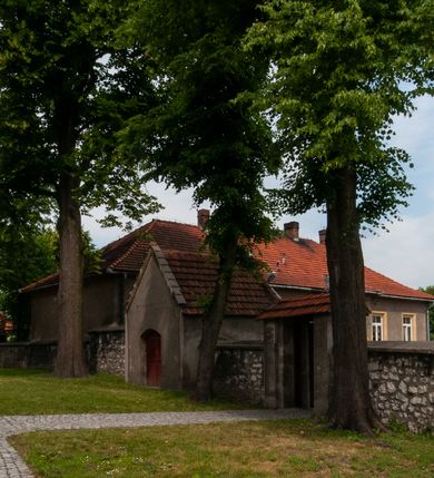 Zdjęcie nr 18: Kościół orientowany, murowany, jednonawowy z prezbiterium zakończonym wielobocznie. Wschodnia część węższa, prostokątna, zachodnia szersza, trójnawowa, halowa. Do prezbiterium od północy przylega zakrystia, do wschodniej części korpusu przybudówka, od zachodu kruchta. Ściany nawy dzielą pilastry. Prezbiterium sklepione krzyżowo, absyda konchowo z lunetami, nawy kolebkowo z lunetami. Od zachodu chór wsparty na dwóch czworobocznych słupach. Jego parapet jest wybrzuszony w części środkowej, ażurowy, zakończony u dołu listwą wycinaną w formie stylizowanych listków. W prezbiterium jedno okno w kształcie stojącego prostokąta zamknięte łukiem pełnym i jedno ślepe, zamknięte łukiem ostrym. Od strony  północnej do zakrystii dwa okna zamknięte łukiem odcinkowym i cztery prostokątne, dwa okna zamknięte łukiem pełnym do zachodniej części nawy; od strony południowej pięć okien zamkniętych łukiem pełnym. Główne wejście od zachodu, drugie od południa, kolejne do  zakrystii, portal z prezbiterium do zakrystii, z czarnego marmuru. Fasada dwuwieżowa, z kruchtą, do której prowadzi ciąg schodów. Kruchta prostopadłościenna, z dachem dwuspadowym, z portalem w kształcie prostokąta zamkniętego łukiem pełnym na osi między oknami powtarzającymi ten kształt. Nad kondygnacją trójkątny przyczółek z krzyżem łacińskim. Fasada dwukondygnacyjna, z wieżami wtopionymi w lico. Pierwsza kondygnacja gładka, flankowana szkarpami, zamknięta gzymsem, druga również niemal gładka, z zegarem na środku i małymi oknami w partii wież. Na osi trójkątny przyczółek. Elewacje obiega cokół, wspierają szkarpy – najgęściej ustawione wokół prezbiterium. Dachy naw dwuspadowe, nad prezbiterium dach zakończony wielobocznie, nad zakrystią pulpitowy; na kalenicy wieżyczka na sygnaturkę, wieże zakończone rozbudowanymi hełmami. 
We wnętrzu na uwagę zasługują chrzcielnica z czarnego marmuru z XVII wieku, obraz św. Izydora w prawym, bocznym ołtarzu według tradycji pędzla Michała Stachowicza i późnobarokowe ołtarze. Prowadzący do zakrystii portal z czarnego marmuru i ołtarz boczny lewy Ukrzyżowania pochodzą, według niektórych przekazów, z krakowskiego kościoła Wszystkich Świętych. 
