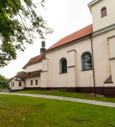 Zdjęcie nr 9: Kościół orientowany, murowany, jednonawowy z prezbiterium zakończonym wielobocznie. Wschodnia część węższa, prostokątna, zachodnia szersza, trójnawowa, halowa. Do prezbiterium od północy przylega zakrystia, do wschodniej części korpusu przybudówka, od zachodu kruchta. Ściany nawy dzielą pilastry. Prezbiterium sklepione krzyżowo, absyda konchowo z lunetami, nawy kolebkowo z lunetami. Od zachodu chór wsparty na dwóch czworobocznych słupach. Jego parapet jest wybrzuszony w części środkowej, ażurowy, zakończony u dołu listwą wycinaną w formie stylizowanych listków. W prezbiterium jedno okno w kształcie stojącego prostokąta zamknięte łukiem pełnym i jedno ślepe, zamknięte łukiem ostrym. Od strony  północnej do zakrystii dwa okna zamknięte łukiem odcinkowym i cztery prostokątne, dwa okna zamknięte łukiem pełnym do zachodniej części nawy; od strony południowej pięć okien zamkniętych łukiem pełnym. Główne wejście od zachodu, drugie od południa, kolejne do  zakrystii, portal z prezbiterium do zakrystii, z czarnego marmuru. Fasada dwuwieżowa, z kruchtą, do której prowadzi ciąg schodów. Kruchta prostopadłościenna, z dachem dwuspadowym, z portalem w kształcie prostokąta zamkniętego łukiem pełnym na osi między oknami powtarzającymi ten kształt. Nad kondygnacją trójkątny przyczółek z krzyżem łacińskim. Fasada dwukondygnacyjna, z wieżami wtopionymi w lico. Pierwsza kondygnacja gładka, flankowana szkarpami, zamknięta gzymsem, druga również niemal gładka, z zegarem na środku i małymi oknami w partii wież. Na osi trójkątny przyczółek. Elewacje obiega cokół, wspierają szkarpy – najgęściej ustawione wokół prezbiterium. Dachy naw dwuspadowe, nad prezbiterium dach zakończony wielobocznie, nad zakrystią pulpitowy; na kalenicy wieżyczka na sygnaturkę, wieże zakończone rozbudowanymi hełmami. 
We wnętrzu na uwagę zasługują chrzcielnica z czarnego marmuru z XVII wieku, obraz św. Izydora w prawym, bocznym ołtarzu według tradycji pędzla Michała Stachowicza i późnobarokowe ołtarze. Prowadzący do zakrystii portal z czarnego marmuru i ołtarz boczny lewy Ukrzyżowania pochodzą, według niektórych przekazów, z krakowskiego kościoła Wszystkich Świętych. 
