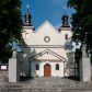 Zdjęcie nr 1: Kościół orientowany, murowany, jednonawowy z prezbiterium zakończonym wielobocznie. Wschodnia część węższa, prostokątna, zachodnia szersza, trójnawowa, halowa. Do prezbiterium od północy przylega zakrystia, do wschodniej części korpusu przybudówka, od zachodu kruchta. Ściany nawy dzielą pilastry. Prezbiterium sklepione krzyżowo, absyda konchowo z lunetami, nawy kolebkowo z lunetami. Od zachodu chór wsparty na dwóch czworobocznych słupach. Jego parapet jest wybrzuszony w części środkowej, ażurowy, zakończony u dołu listwą wycinaną w formie stylizowanych listków. W prezbiterium jedno okno w kształcie stojącego prostokąta zamknięte łukiem pełnym i jedno ślepe, zamknięte łukiem ostrym. Od strony  północnej do zakrystii dwa okna zamknięte łukiem odcinkowym i cztery prostokątne, dwa okna zamknięte łukiem pełnym do zachodniej części nawy; od strony południowej pięć okien zamkniętych łukiem pełnym. Główne wejście od zachodu, drugie od południa, kolejne do  zakrystii, portal z prezbiterium do zakrystii, z czarnego marmuru. Fasada dwuwieżowa, z kruchtą, do której prowadzi ciąg schodów. Kruchta prostopadłościenna, z dachem dwuspadowym, z portalem w kształcie prostokąta zamkniętego łukiem pełnym na osi między oknami powtarzającymi ten kształt. Nad kondygnacją trójkątny przyczółek z krzyżem łacińskim. Fasada dwukondygnacyjna, z wieżami wtopionymi w lico. Pierwsza kondygnacja gładka, flankowana szkarpami, zamknięta gzymsem, druga również niemal gładka, z zegarem na środku i małymi oknami w partii wież. Na osi trójkątny przyczółek. Elewacje obiega cokół, wspierają szkarpy – najgęściej ustawione wokół prezbiterium. Dachy naw dwuspadowe, nad prezbiterium dach zakończony wielobocznie, nad zakrystią pulpitowy; na kalenicy wieżyczka na sygnaturkę, wieże zakończone rozbudowanymi hełmami. 
We wnętrzu na uwagę zasługują chrzcielnica z czarnego marmuru z XVII wieku, obraz św. Izydora w prawym, bocznym ołtarzu według tradycji pędzla Michała Stachowicza i późnobarokowe ołtarze. Prowadzący do zakrystii portal z czarnego marmuru i ołtarz boczny lewy Ukrzyżowania pochodzą, według niektórych przekazów, z krakowskiego kościoła Wszystkich Świętych. 

