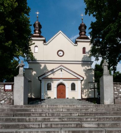 Zdjęcie nr 1: Kościół orientowany, murowany, jednonawowy z prezbiterium zakończonym wielobocznie. Wschodnia część węższa, prostokątna, zachodnia szersza, trójnawowa, halowa. Do prezbiterium od północy przylega zakrystia, do wschodniej części korpusu przybudówka, od zachodu kruchta. Ściany nawy dzielą pilastry. Prezbiterium sklepione krzyżowo, absyda konchowo z lunetami, nawy kolebkowo z lunetami. Od zachodu chór wsparty na dwóch czworobocznych słupach. Jego parapet jest wybrzuszony w części środkowej, ażurowy, zakończony u dołu listwą wycinaną w formie stylizowanych listków. W prezbiterium jedno okno w kształcie stojącego prostokąta zamknięte łukiem pełnym i jedno ślepe, zamknięte łukiem ostrym. Od strony  północnej do zakrystii dwa okna zamknięte łukiem odcinkowym i cztery prostokątne, dwa okna zamknięte łukiem pełnym do zachodniej części nawy; od strony południowej pięć okien zamkniętych łukiem pełnym. Główne wejście od zachodu, drugie od południa, kolejne do  zakrystii, portal z prezbiterium do zakrystii, z czarnego marmuru. Fasada dwuwieżowa, z kruchtą, do której prowadzi ciąg schodów. Kruchta prostopadłościenna, z dachem dwuspadowym, z portalem w kształcie prostokąta zamkniętego łukiem pełnym na osi między oknami powtarzającymi ten kształt. Nad kondygnacją trójkątny przyczółek z krzyżem łacińskim. Fasada dwukondygnacyjna, z wieżami wtopionymi w lico. Pierwsza kondygnacja gładka, flankowana szkarpami, zamknięta gzymsem, druga również niemal gładka, z zegarem na środku i małymi oknami w partii wież. Na osi trójkątny przyczółek. Elewacje obiega cokół, wspierają szkarpy – najgęściej ustawione wokół prezbiterium. Dachy naw dwuspadowe, nad prezbiterium dach zakończony wielobocznie, nad zakrystią pulpitowy; na kalenicy wieżyczka na sygnaturkę, wieże zakończone rozbudowanymi hełmami. 
We wnętrzu na uwagę zasługują chrzcielnica z czarnego marmuru z XVII wieku, obraz św. Izydora w prawym, bocznym ołtarzu według tradycji pędzla Michała Stachowicza i późnobarokowe ołtarze. Prowadzący do zakrystii portal z czarnego marmuru i ołtarz boczny lewy Ukrzyżowania pochodzą, według niektórych przekazów, z krakowskiego kościoła Wszystkich Świętych. 
