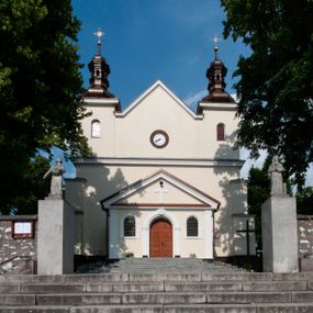 Zdjęcie nr 1: Kościół orientowany, murowany, jednonawowy z prezbiterium zakończonym wielobocznie. Wschodnia część węższa, prostokątna, zachodnia szersza, trójnawowa, halowa. Do prezbiterium od północy przylega zakrystia, do wschodniej części korpusu przybudówka, od zachodu kruchta. Ściany nawy dzielą pilastry. Prezbiterium sklepione krzyżowo, absyda konchowo z lunetami, nawy kolebkowo z lunetami. Od zachodu chór wsparty na dwóch czworobocznych słupach. Jego parapet jest wybrzuszony w części środkowej, ażurowy, zakończony u dołu listwą wycinaną w formie stylizowanych listków. W prezbiterium jedno okno w kształcie stojącego prostokąta zamknięte łukiem pełnym i jedno ślepe, zamknięte łukiem ostrym. Od strony  północnej do zakrystii dwa okna zamknięte łukiem odcinkowym i cztery prostokątne, dwa okna zamknięte łukiem pełnym do zachodniej części nawy; od strony południowej pięć okien zamkniętych łukiem pełnym. Główne wejście od zachodu, drugie od południa, kolejne do  zakrystii, portal z prezbiterium do zakrystii, z czarnego marmuru. Fasada dwuwieżowa, z kruchtą, do której prowadzi ciąg schodów. Kruchta prostopadłościenna, z dachem dwuspadowym, z portalem w kształcie prostokąta zamkniętego łukiem pełnym na osi między oknami powtarzającymi ten kształt. Nad kondygnacją trójkątny przyczółek z krzyżem łacińskim. Fasada dwukondygnacyjna, z wieżami wtopionymi w lico. Pierwsza kondygnacja gładka, flankowana szkarpami, zamknięta gzymsem, druga również niemal gładka, z zegarem na środku i małymi oknami w partii wież. Na osi trójkątny przyczółek. Elewacje obiega cokół, wspierają szkarpy – najgęściej ustawione wokół prezbiterium. Dachy naw dwuspadowe, nad prezbiterium dach zakończony wielobocznie, nad zakrystią pulpitowy; na kalenicy wieżyczka na sygnaturkę, wieże zakończone rozbudowanymi hełmami. 
We wnętrzu na uwagę zasługują chrzcielnica z czarnego marmuru z XVII wieku, obraz św. Izydora w prawym, bocznym ołtarzu według tradycji pędzla Michała Stachowicza i późnobarokowe ołtarze. Prowadzący do zakrystii portal z czarnego marmuru i ołtarz boczny lewy Ukrzyżowania pochodzą, według niektórych przekazów, z krakowskiego kościoła Wszystkich Świętych. 
