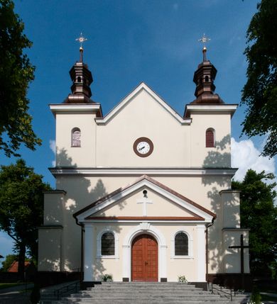 Zdjęcie nr 24: Kościół orientowany, murowany, jednonawowy z prezbiterium zakończonym wielobocznie. Wschodnia część węższa, prostokątna, zachodnia szersza, trójnawowa, halowa. Do prezbiterium od północy przylega zakrystia, do wschodniej części korpusu przybudówka, od zachodu kruchta. Ściany nawy dzielą pilastry. Prezbiterium sklepione krzyżowo, absyda konchowo z lunetami, nawy kolebkowo z lunetami. Od zachodu chór wsparty na dwóch czworobocznych słupach. Jego parapet jest wybrzuszony w części środkowej, ażurowy, zakończony u dołu listwą wycinaną w formie stylizowanych listków. W prezbiterium jedno okno w kształcie stojącego prostokąta zamknięte łukiem pełnym i jedno ślepe, zamknięte łukiem ostrym. Od strony  północnej do zakrystii dwa okna zamknięte łukiem odcinkowym i cztery prostokątne, dwa okna zamknięte łukiem pełnym do zachodniej części nawy; od strony południowej pięć okien zamkniętych łukiem pełnym. Główne wejście od zachodu, drugie od południa, kolejne do  zakrystii, portal z prezbiterium do zakrystii, z czarnego marmuru. Fasada dwuwieżowa, z kruchtą, do której prowadzi ciąg schodów. Kruchta prostopadłościenna, z dachem dwuspadowym, z portalem w kształcie prostokąta zamkniętego łukiem pełnym na osi między oknami powtarzającymi ten kształt. Nad kondygnacją trójkątny przyczółek z krzyżem łacińskim. Fasada dwukondygnacyjna, z wieżami wtopionymi w lico. Pierwsza kondygnacja gładka, flankowana szkarpami, zamknięta gzymsem, druga również niemal gładka, z zegarem na środku i małymi oknami w partii wież. Na osi trójkątny przyczółek. Elewacje obiega cokół, wspierają szkarpy – najgęściej ustawione wokół prezbiterium. Dachy naw dwuspadowe, nad prezbiterium dach zakończony wielobocznie, nad zakrystią pulpitowy; na kalenicy wieżyczka na sygnaturkę, wieże zakończone rozbudowanymi hełmami. 
We wnętrzu na uwagę zasługują chrzcielnica z czarnego marmuru z XVII wieku, obraz św. Izydora w prawym, bocznym ołtarzu według tradycji pędzla Michała Stachowicza i późnobarokowe ołtarze. Prowadzący do zakrystii portal z czarnego marmuru i ołtarz boczny lewy Ukrzyżowania pochodzą, według niektórych przekazów, z krakowskiego kościoła Wszystkich Świętych. 
