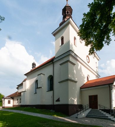 Zdjęcie nr 8: Kościół orientowany, murowany, jednonawowy z prezbiterium zakończonym wielobocznie. Wschodnia część węższa, prostokątna, zachodnia szersza, trójnawowa, halowa. Do prezbiterium od północy przylega zakrystia, do wschodniej części korpusu przybudówka, od zachodu kruchta. Ściany nawy dzielą pilastry. Prezbiterium sklepione krzyżowo, absyda konchowo z lunetami, nawy kolebkowo z lunetami. Od zachodu chór wsparty na dwóch czworobocznych słupach. Jego parapet jest wybrzuszony w części środkowej, ażurowy, zakończony u dołu listwą wycinaną w formie stylizowanych listków. W prezbiterium jedno okno w kształcie stojącego prostokąta zamknięte łukiem pełnym i jedno ślepe, zamknięte łukiem ostrym. Od strony  północnej do zakrystii dwa okna zamknięte łukiem odcinkowym i cztery prostokątne, dwa okna zamknięte łukiem pełnym do zachodniej części nawy; od strony południowej pięć okien zamkniętych łukiem pełnym. Główne wejście od zachodu, drugie od południa, kolejne do  zakrystii, portal z prezbiterium do zakrystii, z czarnego marmuru. Fasada dwuwieżowa, z kruchtą, do której prowadzi ciąg schodów. Kruchta prostopadłościenna, z dachem dwuspadowym, z portalem w kształcie prostokąta zamkniętego łukiem pełnym na osi między oknami powtarzającymi ten kształt. Nad kondygnacją trójkątny przyczółek z krzyżem łacińskim. Fasada dwukondygnacyjna, z wieżami wtopionymi w lico. Pierwsza kondygnacja gładka, flankowana szkarpami, zamknięta gzymsem, druga również niemal gładka, z zegarem na środku i małymi oknami w partii wież. Na osi trójkątny przyczółek. Elewacje obiega cokół, wspierają szkarpy – najgęściej ustawione wokół prezbiterium. Dachy naw dwuspadowe, nad prezbiterium dach zakończony wielobocznie, nad zakrystią pulpitowy; na kalenicy wieżyczka na sygnaturkę, wieże zakończone rozbudowanymi hełmami. 
We wnętrzu na uwagę zasługują chrzcielnica z czarnego marmuru z XVII wieku, obraz św. Izydora w prawym, bocznym ołtarzu według tradycji pędzla Michała Stachowicza i późnobarokowe ołtarze. Prowadzący do zakrystii portal z czarnego marmuru i ołtarz boczny lewy Ukrzyżowania pochodzą, według niektórych przekazów, z krakowskiego kościoła Wszystkich Świętych. 
