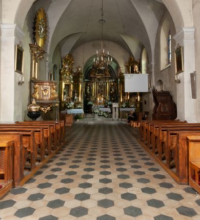 Zdjęcie nr 20: Kościół orientowany, murowany, jednonawowy z prezbiterium zakończonym wielobocznie. Wschodnia część węższa, prostokątna, zachodnia szersza, trójnawowa, halowa. Do prezbiterium od północy przylega zakrystia, do wschodniej części korpusu przybudówka, od zachodu kruchta. Ściany nawy dzielą pilastry. Prezbiterium sklepione krzyżowo, absyda konchowo z lunetami, nawy kolebkowo z lunetami. Od zachodu chór wsparty na dwóch czworobocznych słupach. Jego parapet jest wybrzuszony w części środkowej, ażurowy, zakończony u dołu listwą wycinaną w formie stylizowanych listków. W prezbiterium jedno okno w kształcie stojącego prostokąta zamknięte łukiem pełnym i jedno ślepe, zamknięte łukiem ostrym. Od strony  północnej do zakrystii dwa okna zamknięte łukiem odcinkowym i cztery prostokątne, dwa okna zamknięte łukiem pełnym do zachodniej części nawy; od strony południowej pięć okien zamkniętych łukiem pełnym. Główne wejście od zachodu, drugie od południa, kolejne do  zakrystii, portal z prezbiterium do zakrystii, z czarnego marmuru. Fasada dwuwieżowa, z kruchtą, do której prowadzi ciąg schodów. Kruchta prostopadłościenna, z dachem dwuspadowym, z portalem w kształcie prostokąta zamkniętego łukiem pełnym na osi między oknami powtarzającymi ten kształt. Nad kondygnacją trójkątny przyczółek z krzyżem łacińskim. Fasada dwukondygnacyjna, z wieżami wtopionymi w lico. Pierwsza kondygnacja gładka, flankowana szkarpami, zamknięta gzymsem, druga również niemal gładka, z zegarem na środku i małymi oknami w partii wież. Na osi trójkątny przyczółek. Elewacje obiega cokół, wspierają szkarpy – najgęściej ustawione wokół prezbiterium. Dachy naw dwuspadowe, nad prezbiterium dach zakończony wielobocznie, nad zakrystią pulpitowy; na kalenicy wieżyczka na sygnaturkę, wieże zakończone rozbudowanymi hełmami. 
We wnętrzu na uwagę zasługują chrzcielnica z czarnego marmuru z XVII wieku, obraz św. Izydora w prawym, bocznym ołtarzu według tradycji pędzla Michała Stachowicza i późnobarokowe ołtarze. Prowadzący do zakrystii portal z czarnego marmuru i ołtarz boczny lewy Ukrzyżowania pochodzą, według niektórych przekazów, z krakowskiego kościoła Wszystkich Świętych. 
