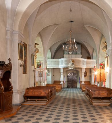 Zdjęcie nr 28: Kościół orientowany, murowany, jednonawowy z prezbiterium zakończonym wielobocznie. Wschodnia część węższa, prostokątna, zachodnia szersza, trójnawowa, halowa. Do prezbiterium od północy przylega zakrystia, do wschodniej części korpusu przybudówka, od zachodu kruchta. Ściany nawy dzielą pilastry. Prezbiterium sklepione krzyżowo, absyda konchowo z lunetami, nawy kolebkowo z lunetami. Od zachodu chór wsparty na dwóch czworobocznych słupach. Jego parapet jest wybrzuszony w części środkowej, ażurowy, zakończony u dołu listwą wycinaną w formie stylizowanych listków. W prezbiterium jedno okno w kształcie stojącego prostokąta zamknięte łukiem pełnym i jedno ślepe, zamknięte łukiem ostrym. Od strony  północnej do zakrystii dwa okna zamknięte łukiem odcinkowym i cztery prostokątne, dwa okna zamknięte łukiem pełnym do zachodniej części nawy; od strony południowej pięć okien zamkniętych łukiem pełnym. Główne wejście od zachodu, drugie od południa, kolejne do  zakrystii, portal z prezbiterium do zakrystii, z czarnego marmuru. Fasada dwuwieżowa, z kruchtą, do której prowadzi ciąg schodów. Kruchta prostopadłościenna, z dachem dwuspadowym, z portalem w kształcie prostokąta zamkniętego łukiem pełnym na osi między oknami powtarzającymi ten kształt. Nad kondygnacją trójkątny przyczółek z krzyżem łacińskim. Fasada dwukondygnacyjna, z wieżami wtopionymi w lico. Pierwsza kondygnacja gładka, flankowana szkarpami, zamknięta gzymsem, druga również niemal gładka, z zegarem na środku i małymi oknami w partii wież. Na osi trójkątny przyczółek. Elewacje obiega cokół, wspierają szkarpy – najgęściej ustawione wokół prezbiterium. Dachy naw dwuspadowe, nad prezbiterium dach zakończony wielobocznie, nad zakrystią pulpitowy; na kalenicy wieżyczka na sygnaturkę, wieże zakończone rozbudowanymi hełmami. 
We wnętrzu na uwagę zasługują chrzcielnica z czarnego marmuru z XVII wieku, obraz św. Izydora w prawym, bocznym ołtarzu według tradycji pędzla Michała Stachowicza i późnobarokowe ołtarze. Prowadzący do zakrystii portal z czarnego marmuru i ołtarz boczny lewy Ukrzyżowania pochodzą, według niektórych przekazów, z krakowskiego kościoła Wszystkich Świętych. 
