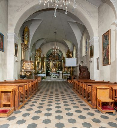 Zdjęcie nr 21: Kościół orientowany, murowany, jednonawowy z prezbiterium zakończonym wielobocznie. Wschodnia część węższa, prostokątna, zachodnia szersza, trójnawowa, halowa. Do prezbiterium od północy przylega zakrystia, do wschodniej części korpusu przybudówka, od zachodu kruchta. Ściany nawy dzielą pilastry. Prezbiterium sklepione krzyżowo, absyda konchowo z lunetami, nawy kolebkowo z lunetami. Od zachodu chór wsparty na dwóch czworobocznych słupach. Jego parapet jest wybrzuszony w części środkowej, ażurowy, zakończony u dołu listwą wycinaną w formie stylizowanych listków. W prezbiterium jedno okno w kształcie stojącego prostokąta zamknięte łukiem pełnym i jedno ślepe, zamknięte łukiem ostrym. Od strony  północnej do zakrystii dwa okna zamknięte łukiem odcinkowym i cztery prostokątne, dwa okna zamknięte łukiem pełnym do zachodniej części nawy; od strony południowej pięć okien zamkniętych łukiem pełnym. Główne wejście od zachodu, drugie od południa, kolejne do  zakrystii, portal z prezbiterium do zakrystii, z czarnego marmuru. Fasada dwuwieżowa, z kruchtą, do której prowadzi ciąg schodów. Kruchta prostopadłościenna, z dachem dwuspadowym, z portalem w kształcie prostokąta zamkniętego łukiem pełnym na osi między oknami powtarzającymi ten kształt. Nad kondygnacją trójkątny przyczółek z krzyżem łacińskim. Fasada dwukondygnacyjna, z wieżami wtopionymi w lico. Pierwsza kondygnacja gładka, flankowana szkarpami, zamknięta gzymsem, druga również niemal gładka, z zegarem na środku i małymi oknami w partii wież. Na osi trójkątny przyczółek. Elewacje obiega cokół, wspierają szkarpy – najgęściej ustawione wokół prezbiterium. Dachy naw dwuspadowe, nad prezbiterium dach zakończony wielobocznie, nad zakrystią pulpitowy; na kalenicy wieżyczka na sygnaturkę, wieże zakończone rozbudowanymi hełmami. 
We wnętrzu na uwagę zasługują chrzcielnica z czarnego marmuru z XVII wieku, obraz św. Izydora w prawym, bocznym ołtarzu według tradycji pędzla Michała Stachowicza i późnobarokowe ołtarze. Prowadzący do zakrystii portal z czarnego marmuru i ołtarz boczny lewy Ukrzyżowania pochodzą, według niektórych przekazów, z krakowskiego kościoła Wszystkich Świętych. 
