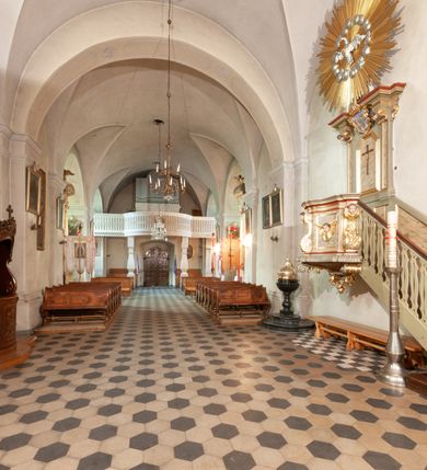 Zdjęcie nr 27: Kościół orientowany, murowany, jednonawowy z prezbiterium zakończonym wielobocznie. Wschodnia część węższa, prostokątna, zachodnia szersza, trójnawowa, halowa. Do prezbiterium od północy przylega zakrystia, do wschodniej części korpusu przybudówka, od zachodu kruchta. Ściany nawy dzielą pilastry. Prezbiterium sklepione krzyżowo, absyda konchowo z lunetami, nawy kolebkowo z lunetami. Od zachodu chór wsparty na dwóch czworobocznych słupach. Jego parapet jest wybrzuszony w części środkowej, ażurowy, zakończony u dołu listwą wycinaną w formie stylizowanych listków. W prezbiterium jedno okno w kształcie stojącego prostokąta zamknięte łukiem pełnym i jedno ślepe, zamknięte łukiem ostrym. Od strony  północnej do zakrystii dwa okna zamknięte łukiem odcinkowym i cztery prostokątne, dwa okna zamknięte łukiem pełnym do zachodniej części nawy; od strony południowej pięć okien zamkniętych łukiem pełnym. Główne wejście od zachodu, drugie od południa, kolejne do  zakrystii, portal z prezbiterium do zakrystii, z czarnego marmuru. Fasada dwuwieżowa, z kruchtą, do której prowadzi ciąg schodów. Kruchta prostopadłościenna, z dachem dwuspadowym, z portalem w kształcie prostokąta zamkniętego łukiem pełnym na osi między oknami powtarzającymi ten kształt. Nad kondygnacją trójkątny przyczółek z krzyżem łacińskim. Fasada dwukondygnacyjna, z wieżami wtopionymi w lico. Pierwsza kondygnacja gładka, flankowana szkarpami, zamknięta gzymsem, druga również niemal gładka, z zegarem na środku i małymi oknami w partii wież. Na osi trójkątny przyczółek. Elewacje obiega cokół, wspierają szkarpy – najgęściej ustawione wokół prezbiterium. Dachy naw dwuspadowe, nad prezbiterium dach zakończony wielobocznie, nad zakrystią pulpitowy; na kalenicy wieżyczka na sygnaturkę, wieże zakończone rozbudowanymi hełmami. 
We wnętrzu na uwagę zasługują chrzcielnica z czarnego marmuru z XVII wieku, obraz św. Izydora w prawym, bocznym ołtarzu według tradycji pędzla Michała Stachowicza i późnobarokowe ołtarze. Prowadzący do zakrystii portal z czarnego marmuru i ołtarz boczny lewy Ukrzyżowania pochodzą, według niektórych przekazów, z krakowskiego kościoła Wszystkich Świętych. 
