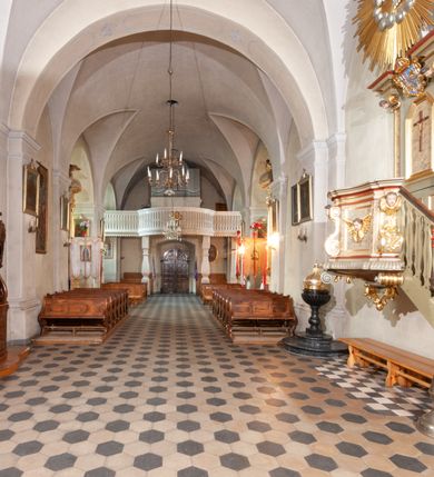 Zdjęcie nr 26: Kościół orientowany, murowany, jednonawowy z prezbiterium zakończonym wielobocznie. Wschodnia część węższa, prostokątna, zachodnia szersza, trójnawowa, halowa. Do prezbiterium od północy przylega zakrystia, do wschodniej części korpusu przybudówka, od zachodu kruchta. Ściany nawy dzielą pilastry. Prezbiterium sklepione krzyżowo, absyda konchowo z lunetami, nawy kolebkowo z lunetami. Od zachodu chór wsparty na dwóch czworobocznych słupach. Jego parapet jest wybrzuszony w części środkowej, ażurowy, zakończony u dołu listwą wycinaną w formie stylizowanych listków. W prezbiterium jedno okno w kształcie stojącego prostokąta zamknięte łukiem pełnym i jedno ślepe, zamknięte łukiem ostrym. Od strony  północnej do zakrystii dwa okna zamknięte łukiem odcinkowym i cztery prostokątne, dwa okna zamknięte łukiem pełnym do zachodniej części nawy; od strony południowej pięć okien zamkniętych łukiem pełnym. Główne wejście od zachodu, drugie od południa, kolejne do  zakrystii, portal z prezbiterium do zakrystii, z czarnego marmuru. Fasada dwuwieżowa, z kruchtą, do której prowadzi ciąg schodów. Kruchta prostopadłościenna, z dachem dwuspadowym, z portalem w kształcie prostokąta zamkniętego łukiem pełnym na osi między oknami powtarzającymi ten kształt. Nad kondygnacją trójkątny przyczółek z krzyżem łacińskim. Fasada dwukondygnacyjna, z wieżami wtopionymi w lico. Pierwsza kondygnacja gładka, flankowana szkarpami, zamknięta gzymsem, druga również niemal gładka, z zegarem na środku i małymi oknami w partii wież. Na osi trójkątny przyczółek. Elewacje obiega cokół, wspierają szkarpy – najgęściej ustawione wokół prezbiterium. Dachy naw dwuspadowe, nad prezbiterium dach zakończony wielobocznie, nad zakrystią pulpitowy; na kalenicy wieżyczka na sygnaturkę, wieże zakończone rozbudowanymi hełmami. 
We wnętrzu na uwagę zasługują chrzcielnica z czarnego marmuru z XVII wieku, obraz św. Izydora w prawym, bocznym ołtarzu według tradycji pędzla Michała Stachowicza i późnobarokowe ołtarze. Prowadzący do zakrystii portal z czarnego marmuru i ołtarz boczny lewy Ukrzyżowania pochodzą, według niektórych przekazów, z krakowskiego kościoła Wszystkich Świętych. 
