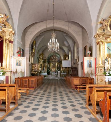 Zdjęcie nr 23: Kościół orientowany, murowany, jednonawowy z prezbiterium zakończonym wielobocznie. Wschodnia część węższa, prostokątna, zachodnia szersza, trójnawowa, halowa. Do prezbiterium od północy przylega zakrystia, do wschodniej części korpusu przybudówka, od zachodu kruchta. Ściany nawy dzielą pilastry. Prezbiterium sklepione krzyżowo, absyda konchowo z lunetami, nawy kolebkowo z lunetami. Od zachodu chór wsparty na dwóch czworobocznych słupach. Jego parapet jest wybrzuszony w części środkowej, ażurowy, zakończony u dołu listwą wycinaną w formie stylizowanych listków. W prezbiterium jedno okno w kształcie stojącego prostokąta zamknięte łukiem pełnym i jedno ślepe, zamknięte łukiem ostrym. Od strony  północnej do zakrystii dwa okna zamknięte łukiem odcinkowym i cztery prostokątne, dwa okna zamknięte łukiem pełnym do zachodniej części nawy; od strony południowej pięć okien zamkniętych łukiem pełnym. Główne wejście od zachodu, drugie od południa, kolejne do  zakrystii, portal z prezbiterium do zakrystii, z czarnego marmuru. Fasada dwuwieżowa, z kruchtą, do której prowadzi ciąg schodów. Kruchta prostopadłościenna, z dachem dwuspadowym, z portalem w kształcie prostokąta zamkniętego łukiem pełnym na osi między oknami powtarzającymi ten kształt. Nad kondygnacją trójkątny przyczółek z krzyżem łacińskim. Fasada dwukondygnacyjna, z wieżami wtopionymi w lico. Pierwsza kondygnacja gładka, flankowana szkarpami, zamknięta gzymsem, druga również niemal gładka, z zegarem na środku i małymi oknami w partii wież. Na osi trójkątny przyczółek. Elewacje obiega cokół, wspierają szkarpy – najgęściej ustawione wokół prezbiterium. Dachy naw dwuspadowe, nad prezbiterium dach zakończony wielobocznie, nad zakrystią pulpitowy; na kalenicy wieżyczka na sygnaturkę, wieże zakończone rozbudowanymi hełmami. 
We wnętrzu na uwagę zasługują chrzcielnica z czarnego marmuru z XVII wieku, obraz św. Izydora w prawym, bocznym ołtarzu według tradycji pędzla Michała Stachowicza i późnobarokowe ołtarze. Prowadzący do zakrystii portal z czarnego marmuru i ołtarz boczny lewy Ukrzyżowania pochodzą, według niektórych przekazów, z krakowskiego kościoła Wszystkich Świętych. 
