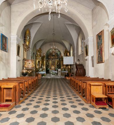 Zdjęcie nr 25: Kościół orientowany, murowany, jednonawowy z prezbiterium zakończonym wielobocznie. Wschodnia część węższa, prostokątna, zachodnia szersza, trójnawowa, halowa. Do prezbiterium od północy przylega zakrystia, do wschodniej części korpusu przybudówka, od zachodu kruchta. Ściany nawy dzielą pilastry. Prezbiterium sklepione krzyżowo, absyda konchowo z lunetami, nawy kolebkowo z lunetami. Od zachodu chór wsparty na dwóch czworobocznych słupach. Jego parapet jest wybrzuszony w części środkowej, ażurowy, zakończony u dołu listwą wycinaną w formie stylizowanych listków. W prezbiterium jedno okno w kształcie stojącego prostokąta zamknięte łukiem pełnym i jedno ślepe, zamknięte łukiem ostrym. Od strony  północnej do zakrystii dwa okna zamknięte łukiem odcinkowym i cztery prostokątne, dwa okna zamknięte łukiem pełnym do zachodniej części nawy; od strony południowej pięć okien zamkniętych łukiem pełnym. Główne wejście od zachodu, drugie od południa, kolejne do  zakrystii, portal z prezbiterium do zakrystii, z czarnego marmuru. Fasada dwuwieżowa, z kruchtą, do której prowadzi ciąg schodów. Kruchta prostopadłościenna, z dachem dwuspadowym, z portalem w kształcie prostokąta zamkniętego łukiem pełnym na osi między oknami powtarzającymi ten kształt. Nad kondygnacją trójkątny przyczółek z krzyżem łacińskim. Fasada dwukondygnacyjna, z wieżami wtopionymi w lico. Pierwsza kondygnacja gładka, flankowana szkarpami, zamknięta gzymsem, druga również niemal gładka, z zegarem na środku i małymi oknami w partii wież. Na osi trójkątny przyczółek. Elewacje obiega cokół, wspierają szkarpy – najgęściej ustawione wokół prezbiterium. Dachy naw dwuspadowe, nad prezbiterium dach zakończony wielobocznie, nad zakrystią pulpitowy; na kalenicy wieżyczka na sygnaturkę, wieże zakończone rozbudowanymi hełmami. 
We wnętrzu na uwagę zasługują chrzcielnica z czarnego marmuru z XVII wieku, obraz św. Izydora w prawym, bocznym ołtarzu według tradycji pędzla Michała Stachowicza i późnobarokowe ołtarze. Prowadzący do zakrystii portal z czarnego marmuru i ołtarz boczny lewy Ukrzyżowania pochodzą, według niektórych przekazów, z krakowskiego kościoła Wszystkich Świętych. 
