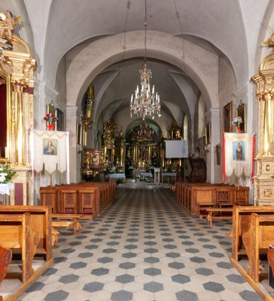 Zdjęcie nr 22: Kościół orientowany, murowany, jednonawowy z prezbiterium zakończonym wielobocznie. Wschodnia część węższa, prostokątna, zachodnia szersza, trójnawowa, halowa. Do prezbiterium od północy przylega zakrystia, do wschodniej części korpusu przybudówka, od zachodu kruchta. Ściany nawy dzielą pilastry. Prezbiterium sklepione krzyżowo, absyda konchowo z lunetami, nawy kolebkowo z lunetami. Od zachodu chór wsparty na dwóch czworobocznych słupach. Jego parapet jest wybrzuszony w części środkowej, ażurowy, zakończony u dołu listwą wycinaną w formie stylizowanych listków. W prezbiterium jedno okno w kształcie stojącego prostokąta zamknięte łukiem pełnym i jedno ślepe, zamknięte łukiem ostrym. Od strony  północnej do zakrystii dwa okna zamknięte łukiem odcinkowym i cztery prostokątne, dwa okna zamknięte łukiem pełnym do zachodniej części nawy; od strony południowej pięć okien zamkniętych łukiem pełnym. Główne wejście od zachodu, drugie od południa, kolejne do  zakrystii, portal z prezbiterium do zakrystii, z czarnego marmuru. Fasada dwuwieżowa, z kruchtą, do której prowadzi ciąg schodów. Kruchta prostopadłościenna, z dachem dwuspadowym, z portalem w kształcie prostokąta zamkniętego łukiem pełnym na osi między oknami powtarzającymi ten kształt. Nad kondygnacją trójkątny przyczółek z krzyżem łacińskim. Fasada dwukondygnacyjna, z wieżami wtopionymi w lico. Pierwsza kondygnacja gładka, flankowana szkarpami, zamknięta gzymsem, druga również niemal gładka, z zegarem na środku i małymi oknami w partii wież. Na osi trójkątny przyczółek. Elewacje obiega cokół, wspierają szkarpy – najgęściej ustawione wokół prezbiterium. Dachy naw dwuspadowe, nad prezbiterium dach zakończony wielobocznie, nad zakrystią pulpitowy; na kalenicy wieżyczka na sygnaturkę, wieże zakończone rozbudowanymi hełmami. 
We wnętrzu na uwagę zasługują chrzcielnica z czarnego marmuru z XVII wieku, obraz św. Izydora w prawym, bocznym ołtarzu według tradycji pędzla Michała Stachowicza i późnobarokowe ołtarze. Prowadzący do zakrystii portal z czarnego marmuru i ołtarz boczny lewy Ukrzyżowania pochodzą, według niektórych przekazów, z krakowskiego kościoła Wszystkich Świętych. 
