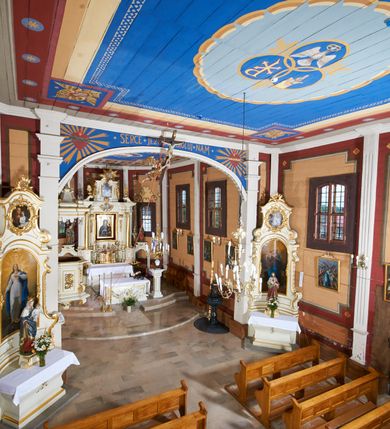 Zdjęcie nr 31: Kościół usytuowany jest w centrum wsi na niewielkim wzniesieniu, orientowany, drewniany, o konstrukcji zrębowej, oszalowany. Jego bryłę tworzy trójbocznie zamknięte prezbiterium, jednonawowy korpus, zakrystia skomunikowana ze skarbcem oraz kruchty od południa i zachodu. Całość pokrywają oddzielne dla nawy i prezbiterium dachy, nad nawą znajduje się wieżyczka na sygnaturkę. Wnętrza niższego, trójbocznie zamkniętego prezbiterium i szerszej, prawie kwadratowej nawy nakryte są stropem. Ściany kościoła zostały podzielone na przęsła kanelowanymi pilastrami ustawionymi na cokołach i zwieńczone profilowanym gzymsem, wyłamującym się na kapitelach. W prezbiterium znajdują się dwa okna od południa i dwa w bocznych ścianach wschodniego zamknięcia; korpus jest oświetlony od południa dwoma oknami. Wszystkie okna zamknięte są łukiem odcinkowym i umieszczone w prostokątnych obramieniach. Przestrzeń między prezbiterium a nawą jest nieznacznie zawężona wydatnymi pilastrami ustawionymi pod arkadą tęczową o łuku koszowym. W środkowym przęśle prezbiterium znajduje się wejście do północnej zakrystii, z profilowanym portalem zamkniętym łukiem trójlistnie ściętym. Na osi ściany południowej umieszczono prostokątny portal, ozdobiony od strony kruchty profilowaniem, a w nadprożu zdwojonym łukiem w  „ośli grzbiet”. Pod nim ornament arkadkowy i wyryta data „1547”. Główne wejście w ścianie zachodniej obejmuje profilowany od strony kruchty portal, który podobnie jak poprzedni zamknięty jest zdwojonym łukiem w „ośli grzbiet”. Chór muzyczny opiera się na dwóch kwadratowych słupach ustawionych diagonalnie (górą dekoracyjnie wycinanych), z parapetem o linii wklęsło-wypukłej. W południowo-zachodnim narożu znajdują się schody na chór osłonięte deskami. Zakrystia jest założona na rzucie prostokąta, przekryta pułapem, z lisicami na ścianie południowej i zachodniej. W osi ściany wschodniej zakrystii umieszczono okno zamknięte łukiem odcinkowym, a w narożu południowo-zachodnim schody na ambonę. W zachodniej ścianie zakrystii znajduje się prostokątne przejście do wąskiego przedsionka i dalej do dawnego skarbca przylegającego do korpusu. Kruchty są założone na rzucie prostokąta, wzdłużnie przylegającego do korpusu i przykryte stropem. Naprzeciw fasady ustawiono wolnostojącą, murowaną dzwonnicę.