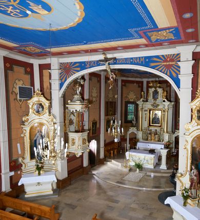 Zdjęcie nr 47: Kościół usytuowany jest w centrum wsi na niewielkim wzniesieniu, orientowany, drewniany, o konstrukcji zrębowej, oszalowany. Jego bryłę tworzy trójbocznie zamknięte prezbiterium, jednonawowy korpus, zakrystia skomunikowana ze skarbcem oraz kruchty od południa i zachodu. Całość pokrywają oddzielne dla nawy i prezbiterium dachy, nad nawą znajduje się wieżyczka na sygnaturkę. Wnętrza niższego, trójbocznie zamkniętego prezbiterium i szerszej, prawie kwadratowej nawy nakryte są stropem. Ściany kościoła zostały podzielone na przęsła kanelowanymi pilastrami ustawionymi na cokołach i zwieńczone profilowanym gzymsem, wyłamującym się na kapitelach. W prezbiterium znajdują się dwa okna od południa i dwa w bocznych ścianach wschodniego zamknięcia; korpus jest oświetlony od południa dwoma oknami. Wszystkie okna zamknięte są łukiem odcinkowym i umieszczone w prostokątnych obramieniach. Przestrzeń między prezbiterium a nawą jest nieznacznie zawężona wydatnymi pilastrami ustawionymi pod arkadą tęczową o łuku koszowym. W środkowym przęśle prezbiterium znajduje się wejście do północnej zakrystii, z profilowanym portalem zamkniętym łukiem trójlistnie ściętym. Na osi ściany południowej umieszczono prostokątny portal, ozdobiony od strony kruchty profilowaniem, a w nadprożu zdwojonym łukiem w  „ośli grzbiet”. Pod nim ornament arkadkowy i wyryta data „1547”. Główne wejście w ścianie zachodniej obejmuje profilowany od strony kruchty portal, który podobnie jak poprzedni zamknięty jest zdwojonym łukiem w „ośli grzbiet”. Chór muzyczny opiera się na dwóch kwadratowych słupach ustawionych diagonalnie (górą dekoracyjnie wycinanych), z parapetem o linii wklęsło-wypukłej. W południowo-zachodnim narożu znajdują się schody na chór osłonięte deskami. Zakrystia jest założona na rzucie prostokąta, przekryta pułapem, z lisicami na ścianie południowej i zachodniej. W osi ściany wschodniej zakrystii umieszczono okno zamknięte łukiem odcinkowym, a w narożu południowo-zachodnim schody na ambonę. W zachodniej ścianie zakrystii znajduje się prostokątne przejście do wąskiego przedsionka i dalej do dawnego skarbca przylegającego do korpusu. Kruchty są założone na rzucie prostokąta, wzdłużnie przylegającego do korpusu i przykryte stropem. Naprzeciw fasady ustawiono wolnostojącą, murowaną dzwonnicę.