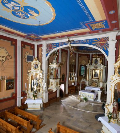 Zdjęcie nr 48: Kościół usytuowany jest w centrum wsi na niewielkim wzniesieniu, orientowany, drewniany, o konstrukcji zrębowej, oszalowany. Jego bryłę tworzy trójbocznie zamknięte prezbiterium, jednonawowy korpus, zakrystia skomunikowana ze skarbcem oraz kruchty od południa i zachodu. Całość pokrywają oddzielne dla nawy i prezbiterium dachy, nad nawą znajduje się wieżyczka na sygnaturkę. Wnętrza niższego, trójbocznie zamkniętego prezbiterium i szerszej, prawie kwadratowej nawy nakryte są stropem. Ściany kościoła zostały podzielone na przęsła kanelowanymi pilastrami ustawionymi na cokołach i zwieńczone profilowanym gzymsem, wyłamującym się na kapitelach. W prezbiterium znajdują się dwa okna od południa i dwa w bocznych ścianach wschodniego zamknięcia; korpus jest oświetlony od południa dwoma oknami. Wszystkie okna zamknięte są łukiem odcinkowym i umieszczone w prostokątnych obramieniach. Przestrzeń między prezbiterium a nawą jest nieznacznie zawężona wydatnymi pilastrami ustawionymi pod arkadą tęczową o łuku koszowym. W środkowym przęśle prezbiterium znajduje się wejście do północnej zakrystii, z profilowanym portalem zamkniętym łukiem trójlistnie ściętym. Na osi ściany południowej umieszczono prostokątny portal, ozdobiony od strony kruchty profilowaniem, a w nadprożu zdwojonym łukiem w  „ośli grzbiet”. Pod nim ornament arkadkowy i wyryta data „1547”. Główne wejście w ścianie zachodniej obejmuje profilowany od strony kruchty portal, który podobnie jak poprzedni zamknięty jest zdwojonym łukiem w „ośli grzbiet”. Chór muzyczny opiera się na dwóch kwadratowych słupach ustawionych diagonalnie (górą dekoracyjnie wycinanych), z parapetem o linii wklęsło-wypukłej. W południowo-zachodnim narożu znajdują się schody na chór osłonięte deskami. Zakrystia jest założona na rzucie prostokąta, przekryta pułapem, z lisicami na ścianie południowej i zachodniej. W osi ściany wschodniej zakrystii umieszczono okno zamknięte łukiem odcinkowym, a w narożu południowo-zachodnim schody na ambonę. W zachodniej ścianie zakrystii znajduje się prostokątne przejście do wąskiego przedsionka i dalej do dawnego skarbca przylegającego do korpusu. Kruchty są założone na rzucie prostokąta, wzdłużnie przylegającego do korpusu i przykryte stropem. Naprzeciw fasady ustawiono wolnostojącą, murowaną dzwonnicę.