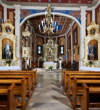 Zdjęcie nr 16: Kościół usytuowany jest w centrum wsi na niewielkim wzniesieniu, orientowany, drewniany, o konstrukcji zrębowej, oszalowany. Jego bryłę tworzy trójbocznie zamknięte prezbiterium, jednonawowy korpus, zakrystia skomunikowana ze skarbcem oraz kruchty od południa i zachodu. Całość pokrywają oddzielne dla nawy i prezbiterium dachy, nad nawą znajduje się wieżyczka na sygnaturkę. Wnętrza niższego, trójbocznie zamkniętego prezbiterium i szerszej, prawie kwadratowej nawy nakryte są stropem. Ściany kościoła zostały podzielone na przęsła kanelowanymi pilastrami ustawionymi na cokołach i zwieńczone profilowanym gzymsem, wyłamującym się na kapitelach. W prezbiterium znajdują się dwa okna od południa i dwa w bocznych ścianach wschodniego zamknięcia; korpus jest oświetlony od południa dwoma oknami. Wszystkie okna zamknięte są łukiem odcinkowym i umieszczone w prostokątnych obramieniach. Przestrzeń między prezbiterium a nawą jest nieznacznie zawężona wydatnymi pilastrami ustawionymi pod arkadą tęczową o łuku koszowym. W środkowym przęśle prezbiterium znajduje się wejście do północnej zakrystii, z profilowanym portalem zamkniętym łukiem trójlistnie ściętym. Na osi ściany południowej umieszczono prostokątny portal, ozdobiony od strony kruchty profilowaniem, a w nadprożu zdwojonym łukiem w  „ośli grzbiet”. Pod nim ornament arkadkowy i wyryta data „1547”. Główne wejście w ścianie zachodniej obejmuje profilowany od strony kruchty portal, który podobnie jak poprzedni zamknięty jest zdwojonym łukiem w „ośli grzbiet”. Chór muzyczny opiera się na dwóch kwadratowych słupach ustawionych diagonalnie (górą dekoracyjnie wycinanych), z parapetem o linii wklęsło-wypukłej. W południowo-zachodnim narożu znajdują się schody na chór osłonięte deskami. Zakrystia jest założona na rzucie prostokąta, przekryta pułapem, z lisicami na ścianie południowej i zachodniej. W osi ściany wschodniej zakrystii umieszczono okno zamknięte łukiem odcinkowym, a w narożu południowo-zachodnim schody na ambonę. W zachodniej ścianie zakrystii znajduje się prostokątne przejście do wąskiego przedsionka i dalej do dawnego skarbca przylegającego do korpusu. Kruchty są założone na rzucie prostokąta, wzdłużnie przylegającego do korpusu i przykryte stropem. Naprzeciw fasady ustawiono wolnostojącą, murowaną dzwonnicę.