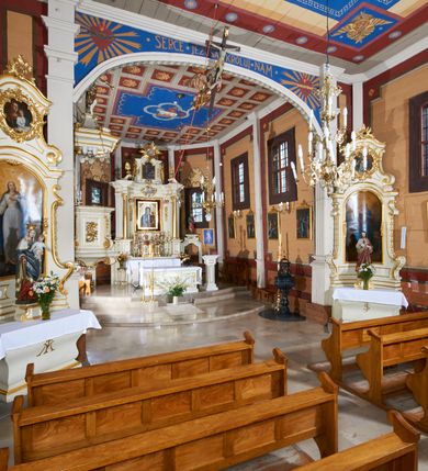 Zdjęcie nr 37: Kościół usytuowany jest w centrum wsi na niewielkim wzniesieniu, orientowany, drewniany, o konstrukcji zrębowej, oszalowany. Jego bryłę tworzy trójbocznie zamknięte prezbiterium, jednonawowy korpus, zakrystia skomunikowana ze skarbcem oraz kruchty od południa i zachodu. Całość pokrywają oddzielne dla nawy i prezbiterium dachy, nad nawą znajduje się wieżyczka na sygnaturkę. Wnętrza niższego, trójbocznie zamkniętego prezbiterium i szerszej, prawie kwadratowej nawy nakryte są stropem. Ściany kościoła zostały podzielone na przęsła kanelowanymi pilastrami ustawionymi na cokołach i zwieńczone profilowanym gzymsem, wyłamującym się na kapitelach. W prezbiterium znajdują się dwa okna od południa i dwa w bocznych ścianach wschodniego zamknięcia; korpus jest oświetlony od południa dwoma oknami. Wszystkie okna zamknięte są łukiem odcinkowym i umieszczone w prostokątnych obramieniach. Przestrzeń między prezbiterium a nawą jest nieznacznie zawężona wydatnymi pilastrami ustawionymi pod arkadą tęczową o łuku koszowym. W środkowym przęśle prezbiterium znajduje się wejście do północnej zakrystii, z profilowanym portalem zamkniętym łukiem trójlistnie ściętym. Na osi ściany południowej umieszczono prostokątny portal, ozdobiony od strony kruchty profilowaniem, a w nadprożu zdwojonym łukiem w  „ośli grzbiet”. Pod nim ornament arkadkowy i wyryta data „1547”. Główne wejście w ścianie zachodniej obejmuje profilowany od strony kruchty portal, który podobnie jak poprzedni zamknięty jest zdwojonym łukiem w „ośli grzbiet”. Chór muzyczny opiera się na dwóch kwadratowych słupach ustawionych diagonalnie (górą dekoracyjnie wycinanych), z parapetem o linii wklęsło-wypukłej. W południowo-zachodnim narożu znajdują się schody na chór osłonięte deskami. Zakrystia jest założona na rzucie prostokąta, przekryta pułapem, z lisicami na ścianie południowej i zachodniej. W osi ściany wschodniej zakrystii umieszczono okno zamknięte łukiem odcinkowym, a w narożu południowo-zachodnim schody na ambonę. W zachodniej ścianie zakrystii znajduje się prostokątne przejście do wąskiego przedsionka i dalej do dawnego skarbca przylegającego do korpusu. Kruchty są założone na rzucie prostokąta, wzdłużnie przylegającego do korpusu i przykryte stropem. Naprzeciw fasady ustawiono wolnostojącą, murowaną dzwonnicę.