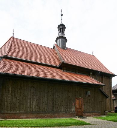 Zdjęcie nr 4: Kościół usytuowany jest w centrum wsi na niewielkim wzniesieniu, orientowany, drewniany, o konstrukcji zrębowej, oszalowany. Jego bryłę tworzy trójbocznie zamknięte prezbiterium, jednonawowy korpus, zakrystia skomunikowana ze skarbcem oraz kruchty od południa i zachodu. Całość pokrywają oddzielne dla nawy i prezbiterium dachy, nad nawą znajduje się wieżyczka na sygnaturkę. Wnętrza niższego, trójbocznie zamkniętego prezbiterium i szerszej, prawie kwadratowej nawy nakryte są stropem. Ściany kościoła zostały podzielone na przęsła kanelowanymi pilastrami ustawionymi na cokołach i zwieńczone profilowanym gzymsem, wyłamującym się na kapitelach. W prezbiterium znajdują się dwa okna od południa i dwa w bocznych ścianach wschodniego zamknięcia; korpus jest oświetlony od południa dwoma oknami. Wszystkie okna zamknięte są łukiem odcinkowym i umieszczone w prostokątnych obramieniach. Przestrzeń między prezbiterium a nawą jest nieznacznie zawężona wydatnymi pilastrami ustawionymi pod arkadą tęczową o łuku koszowym. W środkowym przęśle prezbiterium znajduje się wejście do północnej zakrystii, z profilowanym portalem zamkniętym łukiem trójlistnie ściętym. Na osi ściany południowej umieszczono prostokątny portal, ozdobiony od strony kruchty profilowaniem, a w nadprożu zdwojonym łukiem w  „ośli grzbiet”. Pod nim ornament arkadkowy i wyryta data „1547”. Główne wejście w ścianie zachodniej obejmuje profilowany od strony kruchty portal, który podobnie jak poprzedni zamknięty jest zdwojonym łukiem w „ośli grzbiet”. Chór muzyczny opiera się na dwóch kwadratowych słupach ustawionych diagonalnie (górą dekoracyjnie wycinanych), z parapetem o linii wklęsło-wypukłej. W południowo-zachodnim narożu znajdują się schody na chór osłonięte deskami. Zakrystia jest założona na rzucie prostokąta, przekryta pułapem, z lisicami na ścianie południowej i zachodniej. W osi ściany wschodniej zakrystii umieszczono okno zamknięte łukiem odcinkowym, a w narożu południowo-zachodnim schody na ambonę. W zachodniej ścianie zakrystii znajduje się prostokątne przejście do wąskiego przedsionka i dalej do dawnego skarbca przylegającego do korpusu. Kruchty są założone na rzucie prostokąta, wzdłużnie przylegającego do korpusu i przykryte stropem. Naprzeciw fasady ustawiono wolnostojącą, murowaną dzwonnicę.