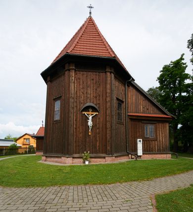 Zdjęcie nr 35: Kościół usytuowany jest w centrum wsi na niewielkim wzniesieniu, orientowany, drewniany, o konstrukcji zrębowej, oszalowany. Jego bryłę tworzy trójbocznie zamknięte prezbiterium, jednonawowy korpus, zakrystia skomunikowana ze skarbcem oraz kruchty od południa i zachodu. Całość pokrywają oddzielne dla nawy i prezbiterium dachy, nad nawą znajduje się wieżyczka na sygnaturkę. Wnętrza niższego, trójbocznie zamkniętego prezbiterium i szerszej, prawie kwadratowej nawy nakryte są stropem. Ściany kościoła zostały podzielone na przęsła kanelowanymi pilastrami ustawionymi na cokołach i zwieńczone profilowanym gzymsem, wyłamującym się na kapitelach. W prezbiterium znajdują się dwa okna od południa i dwa w bocznych ścianach wschodniego zamknięcia; korpus jest oświetlony od południa dwoma oknami. Wszystkie okna zamknięte są łukiem odcinkowym i umieszczone w prostokątnych obramieniach. Przestrzeń między prezbiterium a nawą jest nieznacznie zawężona wydatnymi pilastrami ustawionymi pod arkadą tęczową o łuku koszowym. W środkowym przęśle prezbiterium znajduje się wejście do północnej zakrystii, z profilowanym portalem zamkniętym łukiem trójlistnie ściętym. Na osi ściany południowej umieszczono prostokątny portal, ozdobiony od strony kruchty profilowaniem, a w nadprożu zdwojonym łukiem w  „ośli grzbiet”. Pod nim ornament arkadkowy i wyryta data „1547”. Główne wejście w ścianie zachodniej obejmuje profilowany od strony kruchty portal, który podobnie jak poprzedni zamknięty jest zdwojonym łukiem w „ośli grzbiet”. Chór muzyczny opiera się na dwóch kwadratowych słupach ustawionych diagonalnie (górą dekoracyjnie wycinanych), z parapetem o linii wklęsło-wypukłej. W południowo-zachodnim narożu znajdują się schody na chór osłonięte deskami. Zakrystia jest założona na rzucie prostokąta, przekryta pułapem, z lisicami na ścianie południowej i zachodniej. W osi ściany wschodniej zakrystii umieszczono okno zamknięte łukiem odcinkowym, a w narożu południowo-zachodnim schody na ambonę. W zachodniej ścianie zakrystii znajduje się prostokątne przejście do wąskiego przedsionka i dalej do dawnego skarbca przylegającego do korpusu. Kruchty są założone na rzucie prostokąta, wzdłużnie przylegającego do korpusu i przykryte stropem. Naprzeciw fasady ustawiono wolnostojącą, murowaną dzwonnicę.