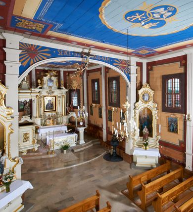 Zdjęcie nr 32: Kościół usytuowany jest w centrum wsi na niewielkim wzniesieniu, orientowany, drewniany, o konstrukcji zrębowej, oszalowany. Jego bryłę tworzy trójbocznie zamknięte prezbiterium, jednonawowy korpus, zakrystia skomunikowana ze skarbcem oraz kruchty od południa i zachodu. Całość pokrywają oddzielne dla nawy i prezbiterium dachy, nad nawą znajduje się wieżyczka na sygnaturkę. Wnętrza niższego, trójbocznie zamkniętego prezbiterium i szerszej, prawie kwadratowej nawy nakryte są stropem. Ściany kościoła zostały podzielone na przęsła kanelowanymi pilastrami ustawionymi na cokołach i zwieńczone profilowanym gzymsem, wyłamującym się na kapitelach. W prezbiterium znajdują się dwa okna od południa i dwa w bocznych ścianach wschodniego zamknięcia; korpus jest oświetlony od południa dwoma oknami. Wszystkie okna zamknięte są łukiem odcinkowym i umieszczone w prostokątnych obramieniach. Przestrzeń między prezbiterium a nawą jest nieznacznie zawężona wydatnymi pilastrami ustawionymi pod arkadą tęczową o łuku koszowym. W środkowym przęśle prezbiterium znajduje się wejście do północnej zakrystii, z profilowanym portalem zamkniętym łukiem trójlistnie ściętym. Na osi ściany południowej umieszczono prostokątny portal, ozdobiony od strony kruchty profilowaniem, a w nadprożu zdwojonym łukiem w  „ośli grzbiet”. Pod nim ornament arkadkowy i wyryta data „1547”. Główne wejście w ścianie zachodniej obejmuje profilowany od strony kruchty portal, który podobnie jak poprzedni zamknięty jest zdwojonym łukiem w „ośli grzbiet”. Chór muzyczny opiera się na dwóch kwadratowych słupach ustawionych diagonalnie (górą dekoracyjnie wycinanych), z parapetem o linii wklęsło-wypukłej. W południowo-zachodnim narożu znajdują się schody na chór osłonięte deskami. Zakrystia jest założona na rzucie prostokąta, przekryta pułapem, z lisicami na ścianie południowej i zachodniej. W osi ściany wschodniej zakrystii umieszczono okno zamknięte łukiem odcinkowym, a w narożu południowo-zachodnim schody na ambonę. W zachodniej ścianie zakrystii znajduje się prostokątne przejście do wąskiego przedsionka i dalej do dawnego skarbca przylegającego do korpusu. Kruchty są założone na rzucie prostokąta, wzdłużnie przylegającego do korpusu i przykryte stropem. Naprzeciw fasady ustawiono wolnostojącą, murowaną dzwonnicę.