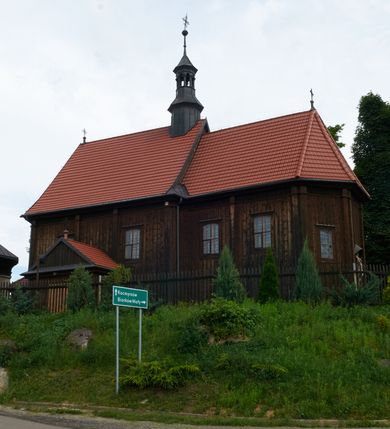 Zdjęcie nr 11: Kościół usytuowany jest w centrum wsi na niewielkim wzniesieniu, orientowany, drewniany, o konstrukcji zrębowej, oszalowany. Jego bryłę tworzy trójbocznie zamknięte prezbiterium, jednonawowy korpus, zakrystia skomunikowana ze skarbcem oraz kruchty od południa i zachodu. Całość pokrywają oddzielne dla nawy i prezbiterium dachy, nad nawą znajduje się wieżyczka na sygnaturkę. Wnętrza niższego, trójbocznie zamkniętego prezbiterium i szerszej, prawie kwadratowej nawy nakryte są stropem. Ściany kościoła zostały podzielone na przęsła kanelowanymi pilastrami ustawionymi na cokołach i zwieńczone profilowanym gzymsem, wyłamującym się na kapitelach. W prezbiterium znajdują się dwa okna od południa i dwa w bocznych ścianach wschodniego zamknięcia; korpus jest oświetlony od południa dwoma oknami. Wszystkie okna zamknięte są łukiem odcinkowym i umieszczone w prostokątnych obramieniach. Przestrzeń między prezbiterium a nawą jest nieznacznie zawężona wydatnymi pilastrami ustawionymi pod arkadą tęczową o łuku koszowym. W środkowym przęśle prezbiterium znajduje się wejście do północnej zakrystii, z profilowanym portalem zamkniętym łukiem trójlistnie ściętym. Na osi ściany południowej umieszczono prostokątny portal, ozdobiony od strony kruchty profilowaniem, a w nadprożu zdwojonym łukiem w  „ośli grzbiet”. Pod nim ornament arkadkowy i wyryta data „1547”. Główne wejście w ścianie zachodniej obejmuje profilowany od strony kruchty portal, który podobnie jak poprzedni zamknięty jest zdwojonym łukiem w „ośli grzbiet”. Chór muzyczny opiera się na dwóch kwadratowych słupach ustawionych diagonalnie (górą dekoracyjnie wycinanych), z parapetem o linii wklęsło-wypukłej. W południowo-zachodnim narożu znajdują się schody na chór osłonięte deskami. Zakrystia jest założona na rzucie prostokąta, przekryta pułapem, z lisicami na ścianie południowej i zachodniej. W osi ściany wschodniej zakrystii umieszczono okno zamknięte łukiem odcinkowym, a w narożu południowo-zachodnim schody na ambonę. W zachodniej ścianie zakrystii znajduje się prostokątne przejście do wąskiego przedsionka i dalej do dawnego skarbca przylegającego do korpusu. Kruchty są założone na rzucie prostokąta, wzdłużnie przylegającego do korpusu i przykryte stropem. Naprzeciw fasady ustawiono wolnostojącą, murowaną dzwonnicę.