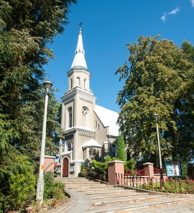 Zdjęcie nr 2: Kościół murowany, tynkowany, orientowany, jednonawowy. 
Prezbiterium prostokątne, zamknięte trójbocznie, od północy przylega zakrystia na planie prostokąta. Nawa szersza od prezbiterium, na rzucie prostokąta, od południa dostawiona kaplica Matki Boskiej na planie prostokąta, od zachodu wieża na planie kwadratu z dwoma aneksami po bokach. 
Prezbiterium dwuprzęsłowe, nawa trójprzęsłowa, nakryte sklepieniami krzyżowo-żebrowymi o gurtach spływających na profilowane wsporniki. Otwór tęczowy w formie półkolistej arkady. Parapet chóru muzycznego drewniany, wsparty na dwóch filarach.  Posadzka z płyt ceramicznych. 
Fasada wieżowa, jednoosiowa, trójkondygnacyjna, zwężająca się ku górze; dwie dolne kondygnacje na planie kwadratu, trzecia ośmioboku. Trzy ściany pierwszej kondygnacji wieży ujęte lizenami, zakończone profilowanym gzymsem z krenelażem oraz daszkiem pulpitowym. Na osi portal w formie stojącego prostokąta zamkniętego łukiem półkolistym, w opasce tynkowej z dwuskrzydłowymi drzwiami. Portal zamknięty od góry i po bokach uskokowym gzymsem z daszkiem pulpitowym. Nad portalem biforium. Trzy ściany drugiej kondygnacji wieży ujęte lizenami, zakończone profilowanym gzymsem z krenelażem oraz daszkiem pulpitowym. Na ścianach ślepe biforia we wnękach w formie stojącego prostokąta zamkniętego łukiem półkolistym. Trzecia kondygnacja zakończona profilowanym gzymsem z kostkowaniem, na ściankach otwory dzwonne w formie stojącego prostokąta zamkniętego łukiem półkolistym, naprzemiennie ślepe i otwarte. Wieża nakryta dachem ostrosłupowym. Po bokach wieży dwukondygnacyjne aneksy na planie wieloboku, przekryte daszkami wielospadowymi. 
Nawa i prezbiterium oszkarpowane w narożach jedno i dwuuskokowymi szkarpami nakrytymi daszkami. Na elewacji południowej pięć otworów okiennych w formie stojącego prostokąta zamkniętego łukiem półkolistym, z szerokim rozglifieniem. Na elewacji wschodniej dwa analogiczne okna, na północnej trzy. 
Nawa, kaplica i zakrystia nakryte dachami blaszanymi, dwuspadowymi, prezbiterium pięciospadowym. 