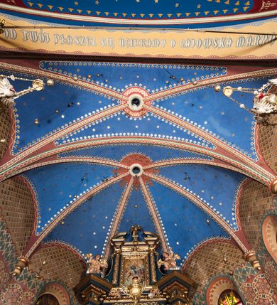 Zdjęcie nr 15: Kościół murowany, tynkowany, orientowany, jednonawowy. 
Prezbiterium prostokątne, zamknięte trójbocznie, od północy przylega zakrystia na planie prostokąta. Nawa szersza od prezbiterium, na rzucie prostokąta, od południa dostawiona kaplica Matki Boskiej na planie prostokąta, od zachodu wieża na planie kwadratu z dwoma aneksami po bokach. 
Prezbiterium dwuprzęsłowe, nawa trójprzęsłowa, nakryte sklepieniami krzyżowo-żebrowymi o gurtach spływających na profilowane wsporniki. Otwór tęczowy w formie półkolistej arkady. Parapet chóru muzycznego drewniany, wsparty na dwóch filarach.  Posadzka z płyt ceramicznych. 
Fasada wieżowa, jednoosiowa, trójkondygnacyjna, zwężająca się ku górze; dwie dolne kondygnacje na planie kwadratu, trzecia ośmioboku. Trzy ściany pierwszej kondygnacji wieży ujęte lizenami, zakończone profilowanym gzymsem z krenelażem oraz daszkiem pulpitowym. Na osi portal w formie stojącego prostokąta zamkniętego łukiem półkolistym, w opasce tynkowej z dwuskrzydłowymi drzwiami. Portal zamknięty od góry i po bokach uskokowym gzymsem z daszkiem pulpitowym. Nad portalem biforium. Trzy ściany drugiej kondygnacji wieży ujęte lizenami, zakończone profilowanym gzymsem z krenelażem oraz daszkiem pulpitowym. Na ścianach ślepe biforia we wnękach w formie stojącego prostokąta zamkniętego łukiem półkolistym. Trzecia kondygnacja zakończona profilowanym gzymsem z kostkowaniem, na ściankach otwory dzwonne w formie stojącego prostokąta zamkniętego łukiem półkolistym, naprzemiennie ślepe i otwarte. Wieża nakryta dachem ostrosłupowym. Po bokach wieży dwukondygnacyjne aneksy na planie wieloboku, przekryte daszkami wielospadowymi. 
Nawa i prezbiterium oszkarpowane w narożach jedno i dwuuskokowymi szkarpami nakrytymi daszkami. Na elewacji południowej pięć otworów okiennych w formie stojącego prostokąta zamkniętego łukiem półkolistym, z szerokim rozglifieniem. Na elewacji wschodniej dwa analogiczne okna, na północnej trzy. 
Nawa, kaplica i zakrystia nakryte dachami blaszanymi, dwuspadowymi, prezbiterium pięciospadowym. 