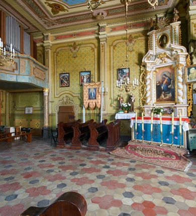 Zdjęcie nr 13: Kościół drewniany o konstrukcji zrębowej, na betonowym podmurowaniu przesłoniętym daszkiem gontowym, kruchta zachodnia o konstrukcji słupowo-ramowej. Elewacje jednolite, szalowane z listwowaniem, wzmocnione lisicami. Więźba dachowa drewniana, krokwiowa. Kościół orientowany, jednonawowy, nawa na rzucie prostokąta zbliżonego do kwadratu, prezbiterium nieco węższe, zakończone trójbocznie. Do wschodniej ściany prezbiterium przylega Ogrójec na rzucie prostokąta, od północy zakrystia na planie zbliżonym do trapezu. Do północnej ściany nawy przylega niewielka kruchta na rzucie prostokąta, od zachodu duża kruchta na planie prostokąta z pomieszczeniem nad nią, ze schodami drabiniastymi na chór, otwarta do nawy trzema dużymi otworami o wykroju prostokątnym. Wnętrze podzielone pilastrami podtrzymującymi architraw i fryz, wyłamane na ich osi. Pomiędzy nawą a prezbiterium prostokątny otwór tęczowy z prostą belką. Parapet chóru muzycznego w zachodniej części nawy, o wklęsło-wypukłym zarysie, podparty przez dwie kolumny i dwie półkolumny o wielobocznych trzonach. Otwory drzwiowe o prostokątnym wykroju zamknięte drzwiami spągowymi w północnej ścianie nawy oraz prezbiterium. Wnętrze nakryte pułapami deskowymi. Posadzka z płyt ceramicznych. 
Elewacja frontowa jednoosiowa, na osi wejście do kruchty z dwuskrzydłowymi drzwiami, w partii szczytu podwójne okno. W elewacji południowej cztery otwory okienne w formie stojącego prostokąta zamkniętego łukiem odcinkowym, dwa w nawie i dwa w prezbiterium oraz prostokątne, podwójne okno w kruchcie zachodniej, z krosnowymi oknami o drobnych podziałach kwaterowych. Elewacja północna z prostokątnym, podwójnym oknem w części kruchty zachodniej oraz z wejściami do kruchty północnej i do zakrystii o dwuskrzydłowych drzwiach. Na ścianie wschodniej prezbiterium Ogrójec w formie głębokiej szalowanej wnęki przesłoniętej daszkiem pulpitowym. Kościół nakryty dachami gontowymi dwuspadowymi, wyższym nad nawą, niższym nad prezbiterium, z kalenicą dekorowaną gontowym grzebieniem, nad zakrystią i kruchtą północną miękko modelowane dachy trójspadowe, kruchta zachodnia nakryta dachem dwuspadowym, półszczytowym. W połowie długości dachu nad nawą od strony prezbiterium wznosi się ponad kalenicą wieżyczka na sygnaturkę, na ośmiobocznym obitym blachą trzonie, z latarnią zwieńczoną niewielkim cebulastym hełmem.

 

