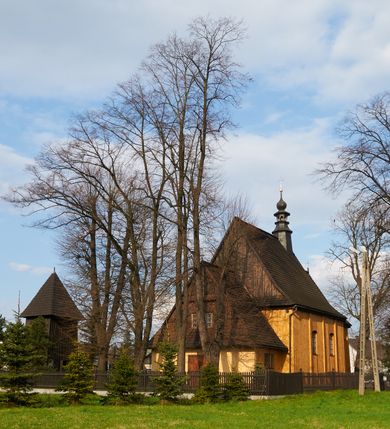 Zdjęcie nr 50: Kościół drewniany o konstrukcji zrębowej, na betonowym podmurowaniu przesłoniętym daszkiem gontowym, kruchta zachodnia o konstrukcji słupowo-ramowej. Elewacje jednolite, szalowane z listwowaniem, wzmocnione lisicami. Więźba dachowa drewniana, krokwiowa. Kościół orientowany, jednonawowy, nawa na rzucie prostokąta zbliżonego do kwadratu, prezbiterium nieco węższe, zakończone trójbocznie. Do wschodniej ściany prezbiterium przylega Ogrójec na rzucie prostokąta, od północy zakrystia na planie zbliżonym do trapezu. Do północnej ściany nawy przylega niewielka kruchta na rzucie prostokąta, od zachodu duża kruchta na planie prostokąta z pomieszczeniem nad nią, ze schodami drabiniastymi na chór, otwarta do nawy trzema dużymi otworami o wykroju prostokątnym. Wnętrze podzielone pilastrami podtrzymującymi architraw i fryz, wyłamane na ich osi. Pomiędzy nawą a prezbiterium prostokątny otwór tęczowy z prostą belką. Parapet chóru muzycznego w zachodniej części nawy, o wklęsło-wypukłym zarysie, podparty przez dwie kolumny i dwie półkolumny o wielobocznych trzonach. Otwory drzwiowe o prostokątnym wykroju zamknięte drzwiami spągowymi w północnej ścianie nawy oraz prezbiterium. Wnętrze nakryte pułapami deskowymi. Posadzka z płyt ceramicznych. 
Elewacja frontowa jednoosiowa, na osi wejście do kruchty z dwuskrzydłowymi drzwiami, w partii szczytu podwójne okno. W elewacji południowej cztery otwory okienne w formie stojącego prostokąta zamkniętego łukiem odcinkowym, dwa w nawie i dwa w prezbiterium oraz prostokątne, podwójne okno w kruchcie zachodniej, z krosnowymi oknami o drobnych podziałach kwaterowych. Elewacja północna z prostokątnym, podwójnym oknem w części kruchty zachodniej oraz z wejściami do kruchty północnej i do zakrystii o dwuskrzydłowych drzwiach. Na ścianie wschodniej prezbiterium Ogrójec w formie głębokiej szalowanej wnęki przesłoniętej daszkiem pulpitowym. Kościół nakryty dachami gontowymi dwuspadowymi, wyższym nad nawą, niższym nad prezbiterium, z kalenicą dekorowaną gontowym grzebieniem, nad zakrystią i kruchtą północną miękko modelowane dachy trójspadowe, kruchta zachodnia nakryta dachem dwuspadowym, półszczytowym. W połowie długości dachu nad nawą od strony prezbiterium wznosi się ponad kalenicą wieżyczka na sygnaturkę, na ośmiobocznym obitym blachą trzonie, z latarnią zwieńczoną niewielkim cebulastym hełmem.

 

