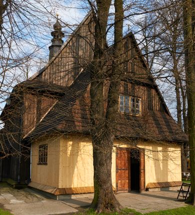 Zdjęcie nr 1: Kościół drewniany o konstrukcji zrębowej, na betonowym podmurowaniu przesłoniętym daszkiem gontowym, kruchta zachodnia o konstrukcji słupowo-ramowej. Elewacje jednolite, szalowane z listwowaniem, wzmocnione lisicami. Więźba dachowa drewniana, krokwiowa. Kościół orientowany, jednonawowy, nawa na rzucie prostokąta zbliżonego do kwadratu, prezbiterium nieco węższe, zakończone trójbocznie. Do wschodniej ściany prezbiterium przylega Ogrójec na rzucie prostokąta, od północy zakrystia na planie zbliżonym do trapezu. Do północnej ściany nawy przylega niewielka kruchta na rzucie prostokąta, od zachodu duża kruchta na planie prostokąta z pomieszczeniem nad nią, ze schodami drabiniastymi na chór, otwarta do nawy trzema dużymi otworami o wykroju prostokątnym. Wnętrze podzielone pilastrami podtrzymującymi architraw i fryz, wyłamane na ich osi. Pomiędzy nawą a prezbiterium prostokątny otwór tęczowy z prostą belką. Parapet chóru muzycznego w zachodniej części nawy, o wklęsło-wypukłym zarysie, podparty przez dwie kolumny i dwie półkolumny o wielobocznych trzonach. Otwory drzwiowe o prostokątnym wykroju zamknięte drzwiami spągowymi w północnej ścianie nawy oraz prezbiterium. Wnętrze nakryte pułapami deskowymi. Posadzka z płyt ceramicznych. 
Elewacja frontowa jednoosiowa, na osi wejście do kruchty z dwuskrzydłowymi drzwiami, w partii szczytu podwójne okno. W elewacji południowej cztery otwory okienne w formie stojącego prostokąta zamkniętego łukiem odcinkowym, dwa w nawie i dwa w prezbiterium oraz prostokątne, podwójne okno w kruchcie zachodniej, z krosnowymi oknami o drobnych podziałach kwaterowych. Elewacja północna z prostokątnym, podwójnym oknem w części kruchty zachodniej oraz z wejściami do kruchty północnej i do zakrystii o dwuskrzydłowych drzwiach. Na ścianie wschodniej prezbiterium Ogrójec w formie głębokiej szalowanej wnęki przesłoniętej daszkiem pulpitowym. Kościół nakryty dachami gontowymi dwuspadowymi, wyższym nad nawą, niższym nad prezbiterium, z kalenicą dekorowaną gontowym grzebieniem, nad zakrystią i kruchtą północną miękko modelowane dachy trójspadowe, kruchta zachodnia nakryta dachem dwuspadowym, półszczytowym. W połowie długości dachu nad nawą od strony prezbiterium wznosi się ponad kalenicą wieżyczka na sygnaturkę, na ośmiobocznym obitym blachą trzonie, z latarnią zwieńczoną niewielkim cebulastym hełmem.

 

