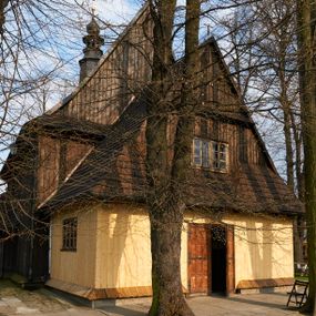Zdjęcie nr 1: Kościół drewniany o konstrukcji zrębowej, na betonowym podmurowaniu przesłoniętym daszkiem gontowym, kruchta zachodnia o konstrukcji słupowo-ramowej. Elewacje jednolite, szalowane z listwowaniem, wzmocnione lisicami. Więźba dachowa drewniana, krokwiowa. Kościół orientowany, jednonawowy, nawa na rzucie prostokąta zbliżonego do kwadratu, prezbiterium nieco węższe, zakończone trójbocznie. Do wschodniej ściany prezbiterium przylega Ogrójec na rzucie prostokąta, od północy zakrystia na planie zbliżonym do trapezu. Do północnej ściany nawy przylega niewielka kruchta na rzucie prostokąta, od zachodu duża kruchta na planie prostokąta z pomieszczeniem nad nią, ze schodami drabiniastymi na chór, otwarta do nawy trzema dużymi otworami o wykroju prostokątnym. Wnętrze podzielone pilastrami podtrzymującymi architraw i fryz, wyłamane na ich osi. Pomiędzy nawą a prezbiterium prostokątny otwór tęczowy z prostą belką. Parapet chóru muzycznego w zachodniej części nawy, o wklęsło-wypukłym zarysie, podparty przez dwie kolumny i dwie półkolumny o wielobocznych trzonach. Otwory drzwiowe o prostokątnym wykroju zamknięte drzwiami spągowymi w północnej ścianie nawy oraz prezbiterium. Wnętrze nakryte pułapami deskowymi. Posadzka z płyt ceramicznych. 
Elewacja frontowa jednoosiowa, na osi wejście do kruchty z dwuskrzydłowymi drzwiami, w partii szczytu podwójne okno. W elewacji południowej cztery otwory okienne w formie stojącego prostokąta zamkniętego łukiem odcinkowym, dwa w nawie i dwa w prezbiterium oraz prostokątne, podwójne okno w kruchcie zachodniej, z krosnowymi oknami o drobnych podziałach kwaterowych. Elewacja północna z prostokątnym, podwójnym oknem w części kruchty zachodniej oraz z wejściami do kruchty północnej i do zakrystii o dwuskrzydłowych drzwiach. Na ścianie wschodniej prezbiterium Ogrójec w formie głębokiej szalowanej wnęki przesłoniętej daszkiem pulpitowym. Kościół nakryty dachami gontowymi dwuspadowymi, wyższym nad nawą, niższym nad prezbiterium, z kalenicą dekorowaną gontowym grzebieniem, nad zakrystią i kruchtą północną miękko modelowane dachy trójspadowe, kruchta zachodnia nakryta dachem dwuspadowym, półszczytowym. W połowie długości dachu nad nawą od strony prezbiterium wznosi się ponad kalenicą wieżyczka na sygnaturkę, na ośmiobocznym obitym blachą trzonie, z latarnią zwieńczoną niewielkim cebulastym hełmem.

 

