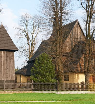 Zdjęcie nr 55: Kościół drewniany o konstrukcji zrębowej, na betonowym podmurowaniu przesłoniętym daszkiem gontowym, kruchta zachodnia o konstrukcji słupowo-ramowej. Elewacje jednolite, szalowane z listwowaniem, wzmocnione lisicami. Więźba dachowa drewniana, krokwiowa. Kościół orientowany, jednonawowy, nawa na rzucie prostokąta zbliżonego do kwadratu, prezbiterium nieco węższe, zakończone trójbocznie. Do wschodniej ściany prezbiterium przylega Ogrójec na rzucie prostokąta, od północy zakrystia na planie zbliżonym do trapezu. Do północnej ściany nawy przylega niewielka kruchta na rzucie prostokąta, od zachodu duża kruchta na planie prostokąta z pomieszczeniem nad nią, ze schodami drabiniastymi na chór, otwarta do nawy trzema dużymi otworami o wykroju prostokątnym. Wnętrze podzielone pilastrami podtrzymującymi architraw i fryz, wyłamane na ich osi. Pomiędzy nawą a prezbiterium prostokątny otwór tęczowy z prostą belką. Parapet chóru muzycznego w zachodniej części nawy, o wklęsło-wypukłym zarysie, podparty przez dwie kolumny i dwie półkolumny o wielobocznych trzonach. Otwory drzwiowe o prostokątnym wykroju zamknięte drzwiami spągowymi w północnej ścianie nawy oraz prezbiterium. Wnętrze nakryte pułapami deskowymi. Posadzka z płyt ceramicznych. 
Elewacja frontowa jednoosiowa, na osi wejście do kruchty z dwuskrzydłowymi drzwiami, w partii szczytu podwójne okno. W elewacji południowej cztery otwory okienne w formie stojącego prostokąta zamkniętego łukiem odcinkowym, dwa w nawie i dwa w prezbiterium oraz prostokątne, podwójne okno w kruchcie zachodniej, z krosnowymi oknami o drobnych podziałach kwaterowych. Elewacja północna z prostokątnym, podwójnym oknem w części kruchty zachodniej oraz z wejściami do kruchty północnej i do zakrystii o dwuskrzydłowych drzwiach. Na ścianie wschodniej prezbiterium Ogrójec w formie głębokiej szalowanej wnęki przesłoniętej daszkiem pulpitowym. Kościół nakryty dachami gontowymi dwuspadowymi, wyższym nad nawą, niższym nad prezbiterium, z kalenicą dekorowaną gontowym grzebieniem, nad zakrystią i kruchtą północną miękko modelowane dachy trójspadowe, kruchta zachodnia nakryta dachem dwuspadowym, półszczytowym. W połowie długości dachu nad nawą od strony prezbiterium wznosi się ponad kalenicą wieżyczka na sygnaturkę, na ośmiobocznym obitym blachą trzonie, z latarnią zwieńczoną niewielkim cebulastym hełmem.

 

