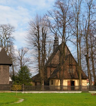 Zdjęcie nr 52: Kościół drewniany o konstrukcji zrębowej, na betonowym podmurowaniu przesłoniętym daszkiem gontowym, kruchta zachodnia o konstrukcji słupowo-ramowej. Elewacje jednolite, szalowane z listwowaniem, wzmocnione lisicami. Więźba dachowa drewniana, krokwiowa. Kościół orientowany, jednonawowy, nawa na rzucie prostokąta zbliżonego do kwadratu, prezbiterium nieco węższe, zakończone trójbocznie. Do wschodniej ściany prezbiterium przylega Ogrójec na rzucie prostokąta, od północy zakrystia na planie zbliżonym do trapezu. Do północnej ściany nawy przylega niewielka kruchta na rzucie prostokąta, od zachodu duża kruchta na planie prostokąta z pomieszczeniem nad nią, ze schodami drabiniastymi na chór, otwarta do nawy trzema dużymi otworami o wykroju prostokątnym. Wnętrze podzielone pilastrami podtrzymującymi architraw i fryz, wyłamane na ich osi. Pomiędzy nawą a prezbiterium prostokątny otwór tęczowy z prostą belką. Parapet chóru muzycznego w zachodniej części nawy, o wklęsło-wypukłym zarysie, podparty przez dwie kolumny i dwie półkolumny o wielobocznych trzonach. Otwory drzwiowe o prostokątnym wykroju zamknięte drzwiami spągowymi w północnej ścianie nawy oraz prezbiterium. Wnętrze nakryte pułapami deskowymi. Posadzka z płyt ceramicznych. 
Elewacja frontowa jednoosiowa, na osi wejście do kruchty z dwuskrzydłowymi drzwiami, w partii szczytu podwójne okno. W elewacji południowej cztery otwory okienne w formie stojącego prostokąta zamkniętego łukiem odcinkowym, dwa w nawie i dwa w prezbiterium oraz prostokątne, podwójne okno w kruchcie zachodniej, z krosnowymi oknami o drobnych podziałach kwaterowych. Elewacja północna z prostokątnym, podwójnym oknem w części kruchty zachodniej oraz z wejściami do kruchty północnej i do zakrystii o dwuskrzydłowych drzwiach. Na ścianie wschodniej prezbiterium Ogrójec w formie głębokiej szalowanej wnęki przesłoniętej daszkiem pulpitowym. Kościół nakryty dachami gontowymi dwuspadowymi, wyższym nad nawą, niższym nad prezbiterium, z kalenicą dekorowaną gontowym grzebieniem, nad zakrystią i kruchtą północną miękko modelowane dachy trójspadowe, kruchta zachodnia nakryta dachem dwuspadowym, półszczytowym. W połowie długości dachu nad nawą od strony prezbiterium wznosi się ponad kalenicą wieżyczka na sygnaturkę, na ośmiobocznym obitym blachą trzonie, z latarnią zwieńczoną niewielkim cebulastym hełmem.

 

