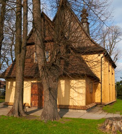 Zdjęcie nr 33: Kościół drewniany o konstrukcji zrębowej, na betonowym podmurowaniu przesłoniętym daszkiem gontowym, kruchta zachodnia o konstrukcji słupowo-ramowej. Elewacje jednolite, szalowane z listwowaniem, wzmocnione lisicami. Więźba dachowa drewniana, krokwiowa. Kościół orientowany, jednonawowy, nawa na rzucie prostokąta zbliżonego do kwadratu, prezbiterium nieco węższe, zakończone trójbocznie. Do wschodniej ściany prezbiterium przylega Ogrójec na rzucie prostokąta, od północy zakrystia na planie zbliżonym do trapezu. Do północnej ściany nawy przylega niewielka kruchta na rzucie prostokąta, od zachodu duża kruchta na planie prostokąta z pomieszczeniem nad nią, ze schodami drabiniastymi na chór, otwarta do nawy trzema dużymi otworami o wykroju prostokątnym. Wnętrze podzielone pilastrami podtrzymującymi architraw i fryz, wyłamane na ich osi. Pomiędzy nawą a prezbiterium prostokątny otwór tęczowy z prostą belką. Parapet chóru muzycznego w zachodniej części nawy, o wklęsło-wypukłym zarysie, podparty przez dwie kolumny i dwie półkolumny o wielobocznych trzonach. Otwory drzwiowe o prostokątnym wykroju zamknięte drzwiami spągowymi w północnej ścianie nawy oraz prezbiterium. Wnętrze nakryte pułapami deskowymi. Posadzka z płyt ceramicznych. 
Elewacja frontowa jednoosiowa, na osi wejście do kruchty z dwuskrzydłowymi drzwiami, w partii szczytu podwójne okno. W elewacji południowej cztery otwory okienne w formie stojącego prostokąta zamkniętego łukiem odcinkowym, dwa w nawie i dwa w prezbiterium oraz prostokątne, podwójne okno w kruchcie zachodniej, z krosnowymi oknami o drobnych podziałach kwaterowych. Elewacja północna z prostokątnym, podwójnym oknem w części kruchty zachodniej oraz z wejściami do kruchty północnej i do zakrystii o dwuskrzydłowych drzwiach. Na ścianie wschodniej prezbiterium Ogrójec w formie głębokiej szalowanej wnęki przesłoniętej daszkiem pulpitowym. Kościół nakryty dachami gontowymi dwuspadowymi, wyższym nad nawą, niższym nad prezbiterium, z kalenicą dekorowaną gontowym grzebieniem, nad zakrystią i kruchtą północną miękko modelowane dachy trójspadowe, kruchta zachodnia nakryta dachem dwuspadowym, półszczytowym. W połowie długości dachu nad nawą od strony prezbiterium wznosi się ponad kalenicą wieżyczka na sygnaturkę, na ośmiobocznym obitym blachą trzonie, z latarnią zwieńczoną niewielkim cebulastym hełmem.

 

