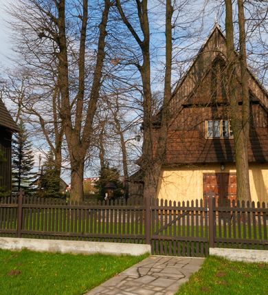 Zdjęcie nr 57: Kościół drewniany o konstrukcji zrębowej, na betonowym podmurowaniu przesłoniętym daszkiem gontowym, kruchta zachodnia o konstrukcji słupowo-ramowej. Elewacje jednolite, szalowane z listwowaniem, wzmocnione lisicami. Więźba dachowa drewniana, krokwiowa. Kościół orientowany, jednonawowy, nawa na rzucie prostokąta zbliżonego do kwadratu, prezbiterium nieco węższe, zakończone trójbocznie. Do wschodniej ściany prezbiterium przylega Ogrójec na rzucie prostokąta, od północy zakrystia na planie zbliżonym do trapezu. Do północnej ściany nawy przylega niewielka kruchta na rzucie prostokąta, od zachodu duża kruchta na planie prostokąta z pomieszczeniem nad nią, ze schodami drabiniastymi na chór, otwarta do nawy trzema dużymi otworami o wykroju prostokątnym. Wnętrze podzielone pilastrami podtrzymującymi architraw i fryz, wyłamane na ich osi. Pomiędzy nawą a prezbiterium prostokątny otwór tęczowy z prostą belką. Parapet chóru muzycznego w zachodniej części nawy, o wklęsło-wypukłym zarysie, podparty przez dwie kolumny i dwie półkolumny o wielobocznych trzonach. Otwory drzwiowe o prostokątnym wykroju zamknięte drzwiami spągowymi w północnej ścianie nawy oraz prezbiterium. Wnętrze nakryte pułapami deskowymi. Posadzka z płyt ceramicznych. 
Elewacja frontowa jednoosiowa, na osi wejście do kruchty z dwuskrzydłowymi drzwiami, w partii szczytu podwójne okno. W elewacji południowej cztery otwory okienne w formie stojącego prostokąta zamkniętego łukiem odcinkowym, dwa w nawie i dwa w prezbiterium oraz prostokątne, podwójne okno w kruchcie zachodniej, z krosnowymi oknami o drobnych podziałach kwaterowych. Elewacja północna z prostokątnym, podwójnym oknem w części kruchty zachodniej oraz z wejściami do kruchty północnej i do zakrystii o dwuskrzydłowych drzwiach. Na ścianie wschodniej prezbiterium Ogrójec w formie głębokiej szalowanej wnęki przesłoniętej daszkiem pulpitowym. Kościół nakryty dachami gontowymi dwuspadowymi, wyższym nad nawą, niższym nad prezbiterium, z kalenicą dekorowaną gontowym grzebieniem, nad zakrystią i kruchtą północną miękko modelowane dachy trójspadowe, kruchta zachodnia nakryta dachem dwuspadowym, półszczytowym. W połowie długości dachu nad nawą od strony prezbiterium wznosi się ponad kalenicą wieżyczka na sygnaturkę, na ośmiobocznym obitym blachą trzonie, z latarnią zwieńczoną niewielkim cebulastym hełmem.

 

