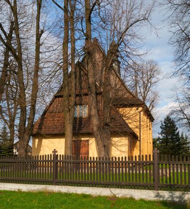 Zdjęcie nr 22: Kościół drewniany o konstrukcji zrębowej, na betonowym podmurowaniu przesłoniętym daszkiem gontowym, kruchta zachodnia o konstrukcji słupowo-ramowej. Elewacje jednolite, szalowane z listwowaniem, wzmocnione lisicami. Więźba dachowa drewniana, krokwiowa. Kościół orientowany, jednonawowy, nawa na rzucie prostokąta zbliżonego do kwadratu, prezbiterium nieco węższe, zakończone trójbocznie. Do wschodniej ściany prezbiterium przylega Ogrójec na rzucie prostokąta, od północy zakrystia na planie zbliżonym do trapezu. Do północnej ściany nawy przylega niewielka kruchta na rzucie prostokąta, od zachodu duża kruchta na planie prostokąta z pomieszczeniem nad nią, ze schodami drabiniastymi na chór, otwarta do nawy trzema dużymi otworami o wykroju prostokątnym. Wnętrze podzielone pilastrami podtrzymującymi architraw i fryz, wyłamane na ich osi. Pomiędzy nawą a prezbiterium prostokątny otwór tęczowy z prostą belką. Parapet chóru muzycznego w zachodniej części nawy, o wklęsło-wypukłym zarysie, podparty przez dwie kolumny i dwie półkolumny o wielobocznych trzonach. Otwory drzwiowe o prostokątnym wykroju zamknięte drzwiami spągowymi w północnej ścianie nawy oraz prezbiterium. Wnętrze nakryte pułapami deskowymi. Posadzka z płyt ceramicznych. 
Elewacja frontowa jednoosiowa, na osi wejście do kruchty z dwuskrzydłowymi drzwiami, w partii szczytu podwójne okno. W elewacji południowej cztery otwory okienne w formie stojącego prostokąta zamkniętego łukiem odcinkowym, dwa w nawie i dwa w prezbiterium oraz prostokątne, podwójne okno w kruchcie zachodniej, z krosnowymi oknami o drobnych podziałach kwaterowych. Elewacja północna z prostokątnym, podwójnym oknem w części kruchty zachodniej oraz z wejściami do kruchty północnej i do zakrystii o dwuskrzydłowych drzwiach. Na ścianie wschodniej prezbiterium Ogrójec w formie głębokiej szalowanej wnęki przesłoniętej daszkiem pulpitowym. Kościół nakryty dachami gontowymi dwuspadowymi, wyższym nad nawą, niższym nad prezbiterium, z kalenicą dekorowaną gontowym grzebieniem, nad zakrystią i kruchtą północną miękko modelowane dachy trójspadowe, kruchta zachodnia nakryta dachem dwuspadowym, półszczytowym. W połowie długości dachu nad nawą od strony prezbiterium wznosi się ponad kalenicą wieżyczka na sygnaturkę, na ośmiobocznym obitym blachą trzonie, z latarnią zwieńczoną niewielkim cebulastym hełmem.

 

